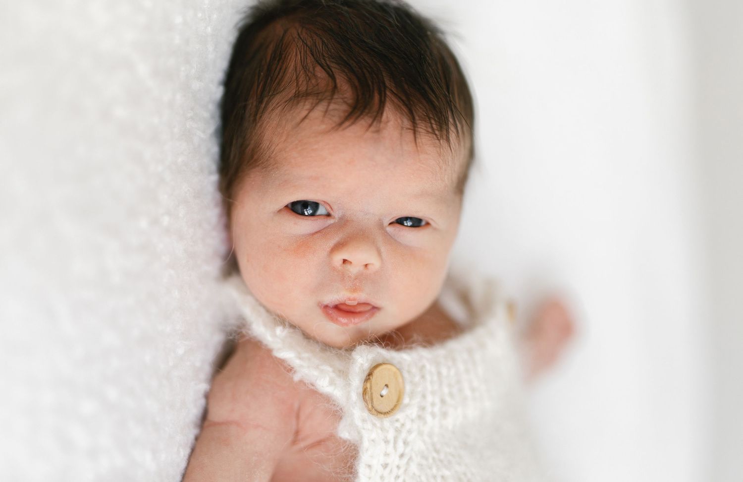 Close-up portrait of newborn with dark hair against white background.