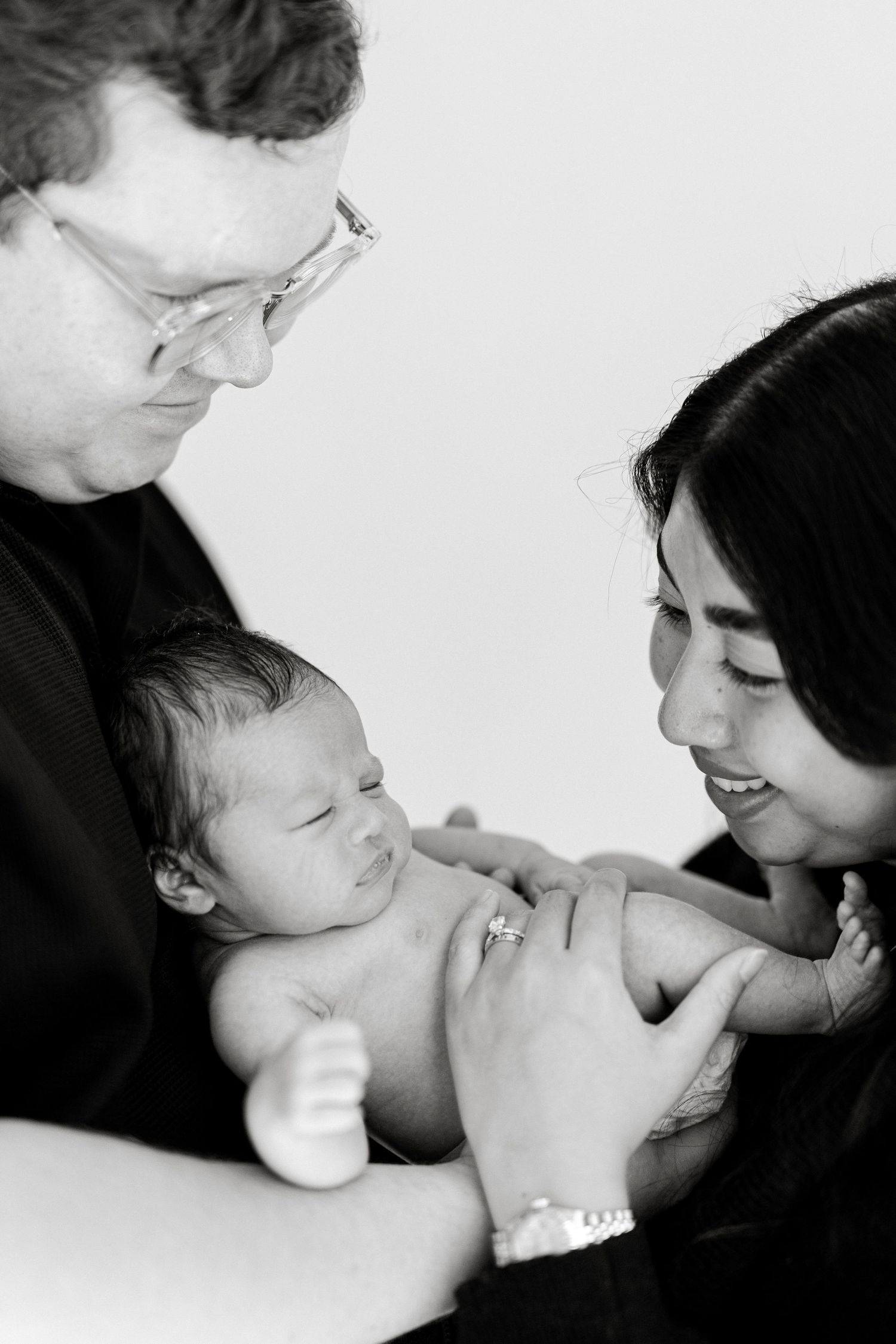 Black and white photo of new parents lovingly holding their newborn baby together.