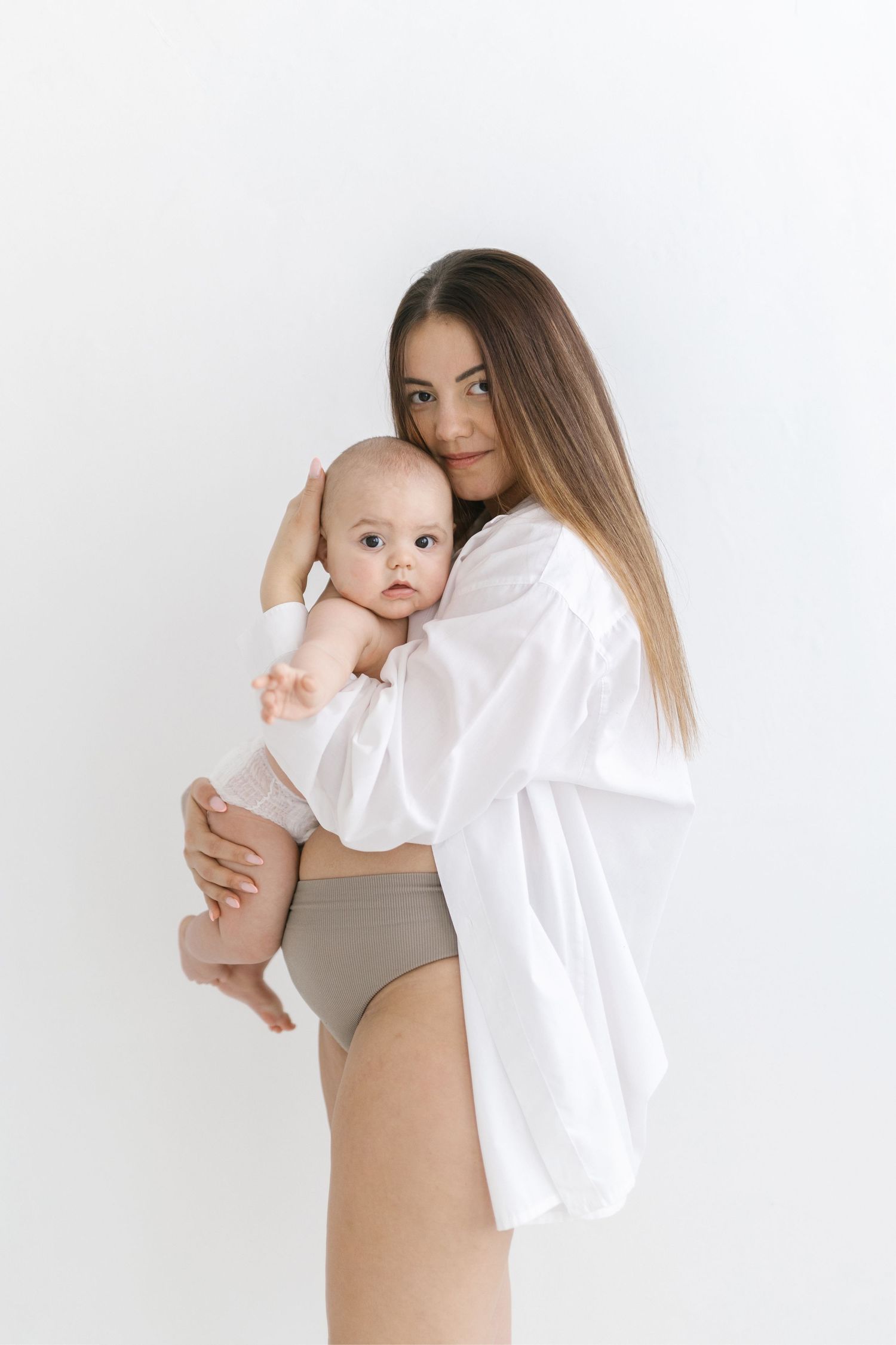Young mother in white shirt holding her baby infant against a clean white background.