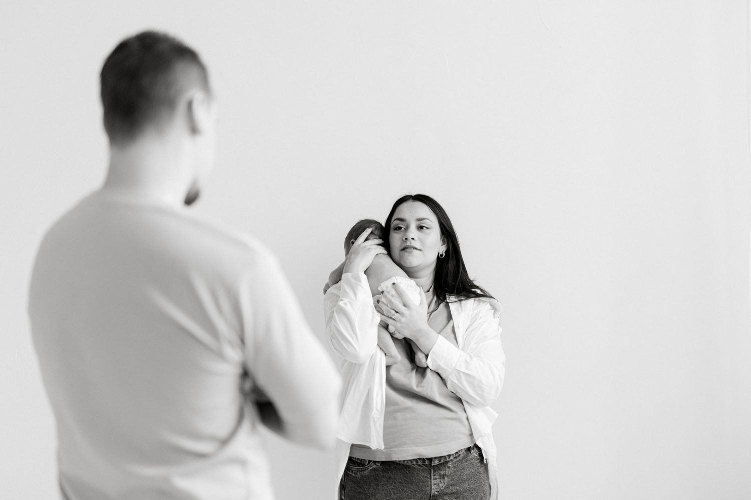 Intimate black and white portrait of parents holding their newborn against a light background.