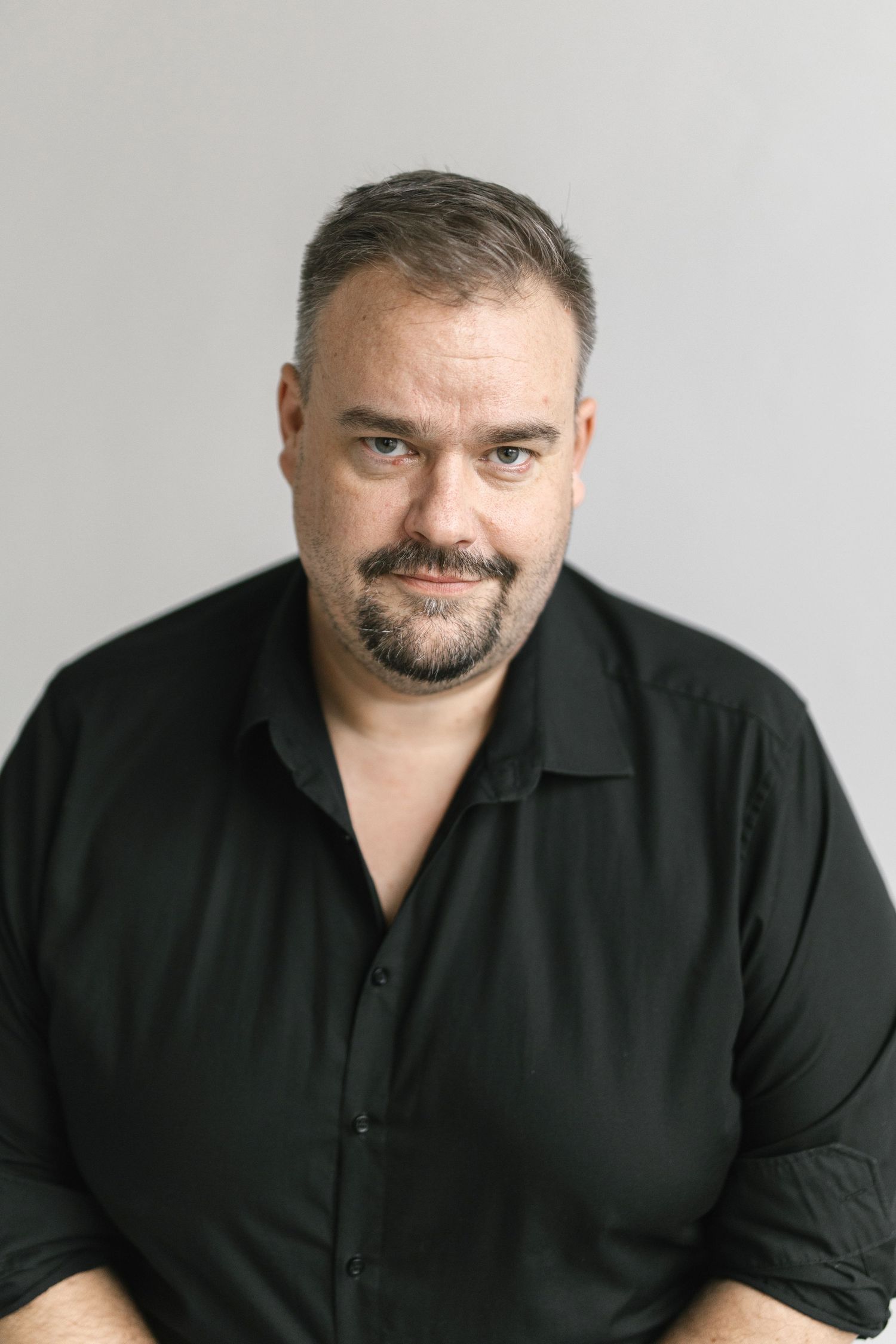 Professional headshot of person in black shirt against light gray background.