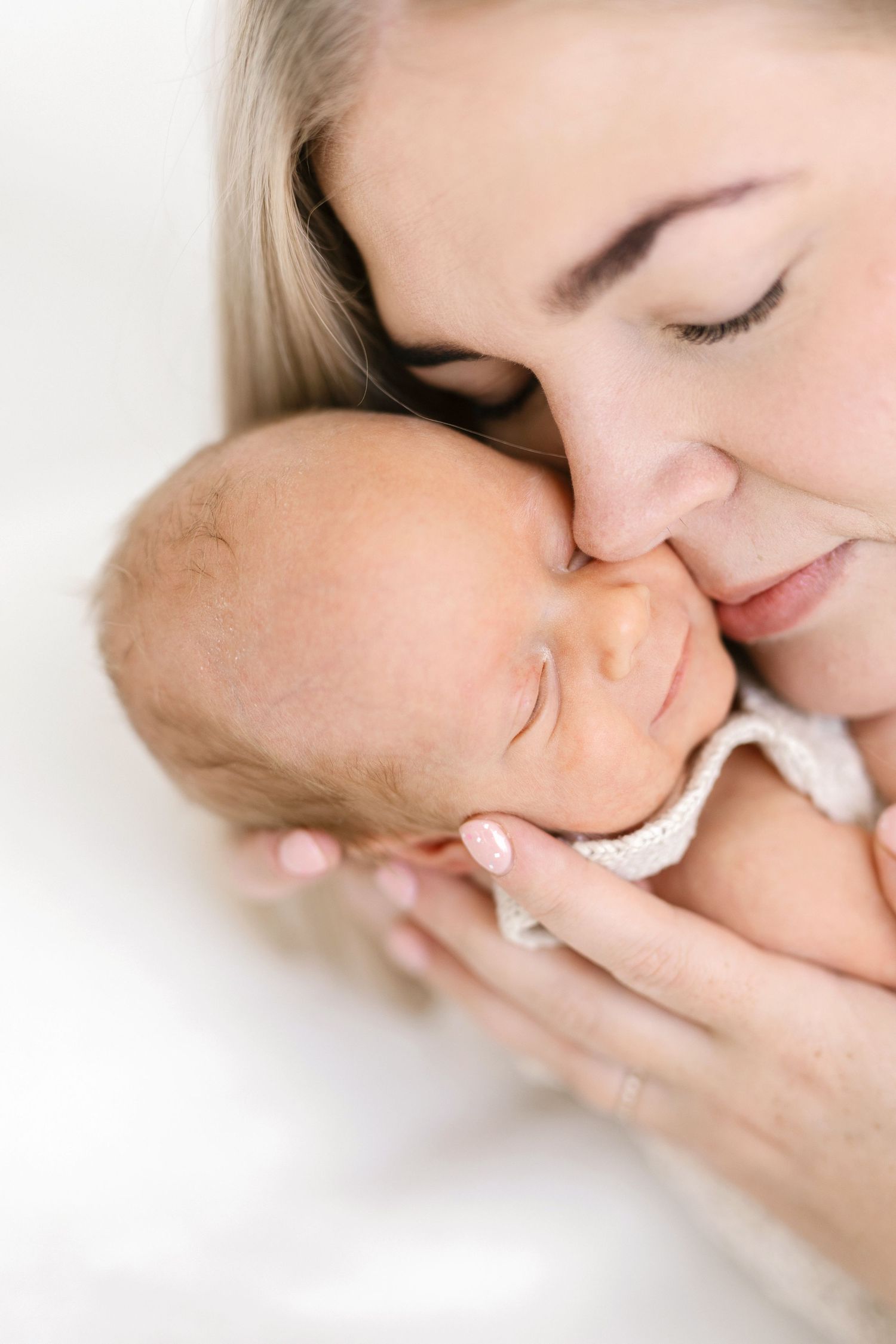 A mother gently kisses her sleeping newborn baby, cradling the infant tenderly in her hands.