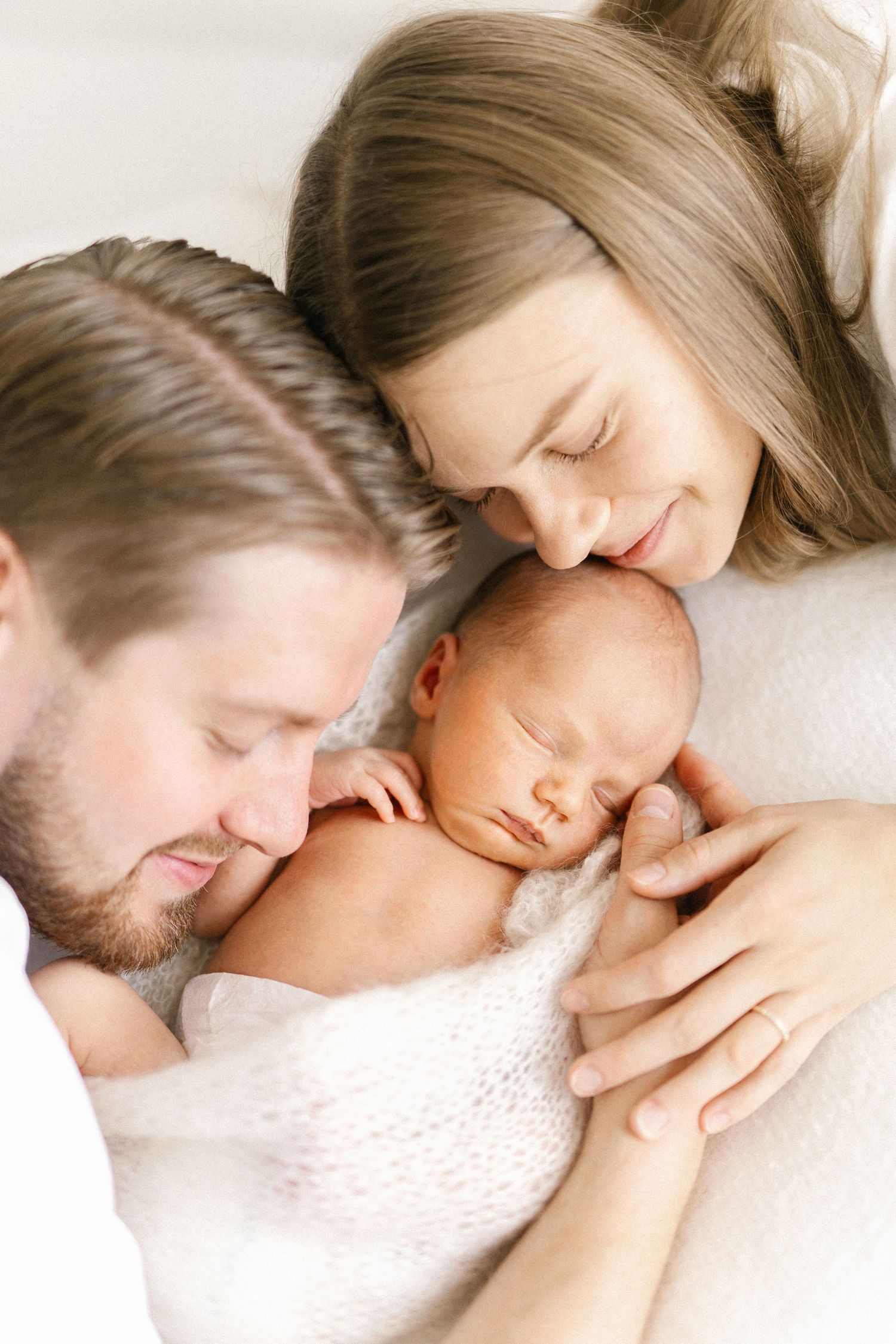 Parents lovingly gazing at their sleeping newborn baby wrapped in a soft white blanket.