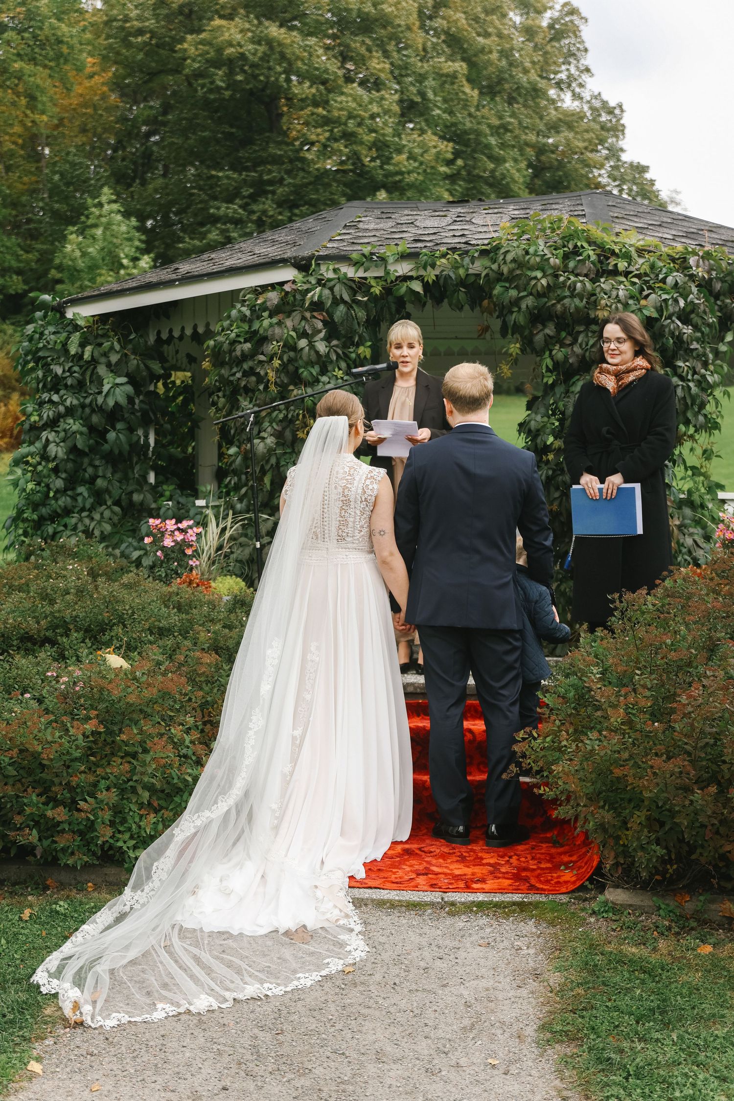 Bride and groom exchange vows at an outdoor garden wedding ceremony with lush green backdrop.