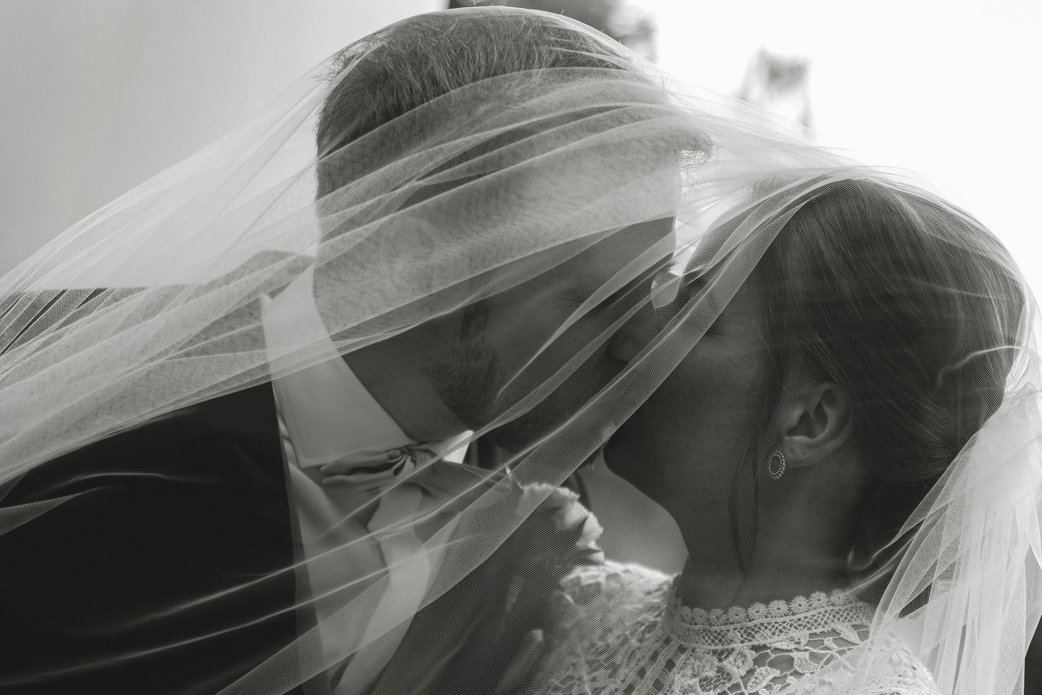 Black and white wedding photo of bride and groom sharing an intimate moment under a flowing veil.