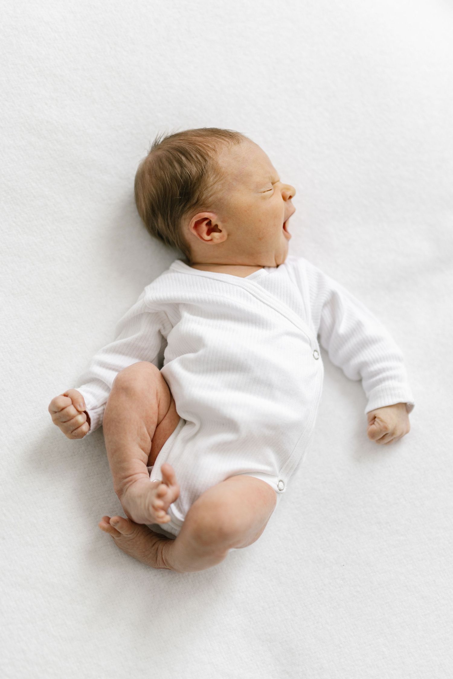 A baby wearing a white onesie lies on a white background in three different positions.