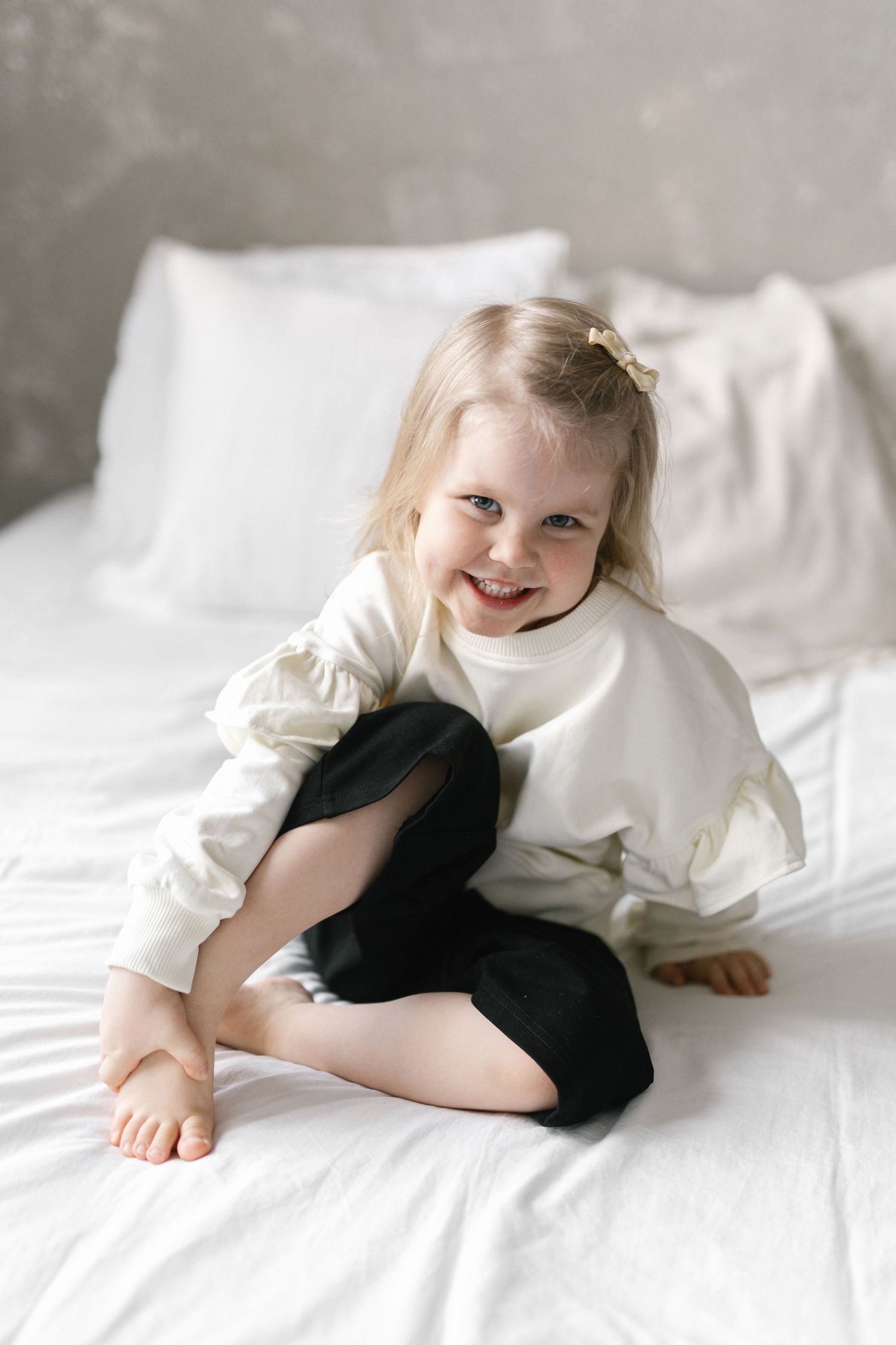 Sweet moments of child playing on white bedding with black stuffed animal.