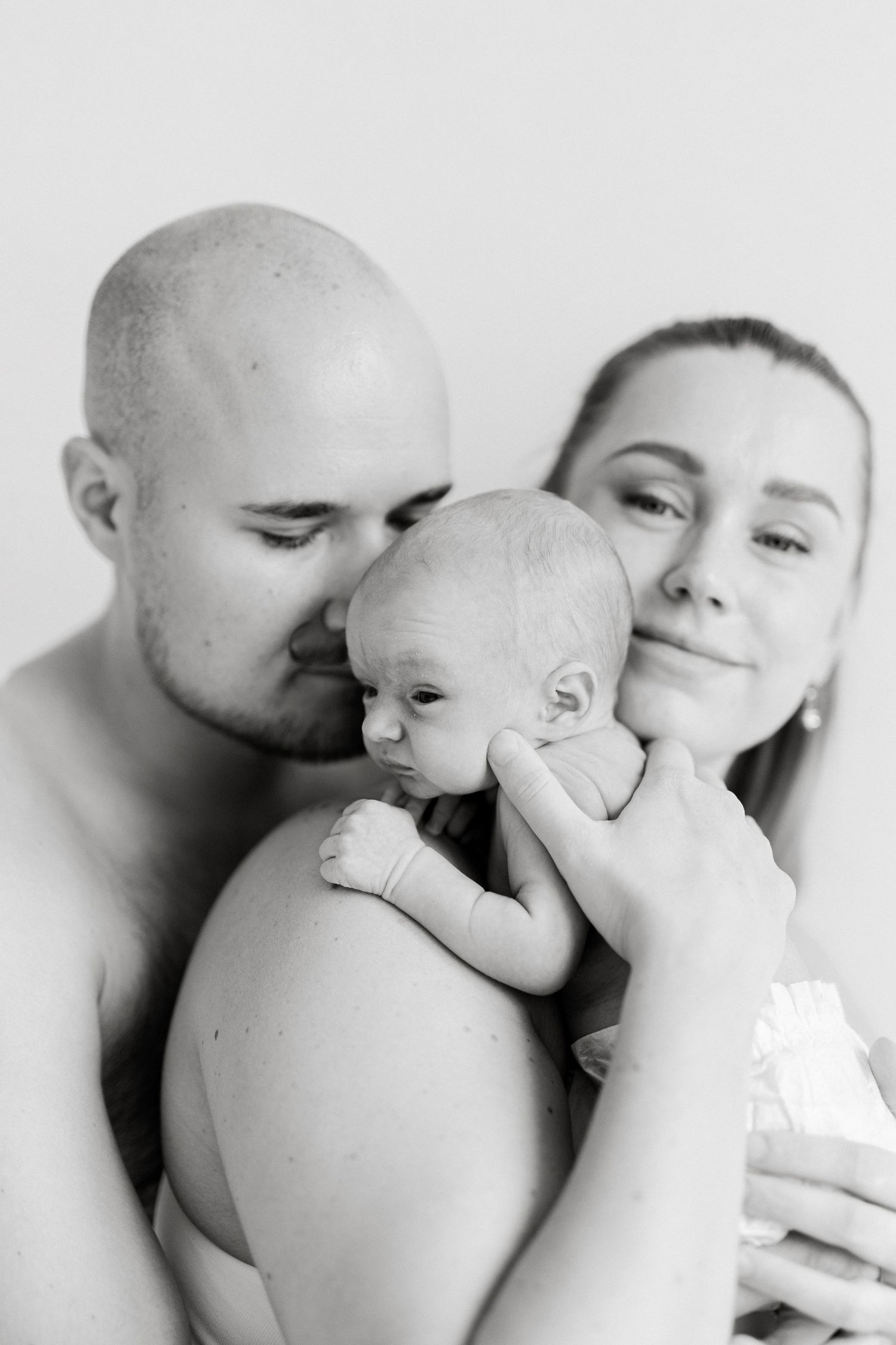 Intimate family portrait showing parents sharing tender kisses with their newborn baby.