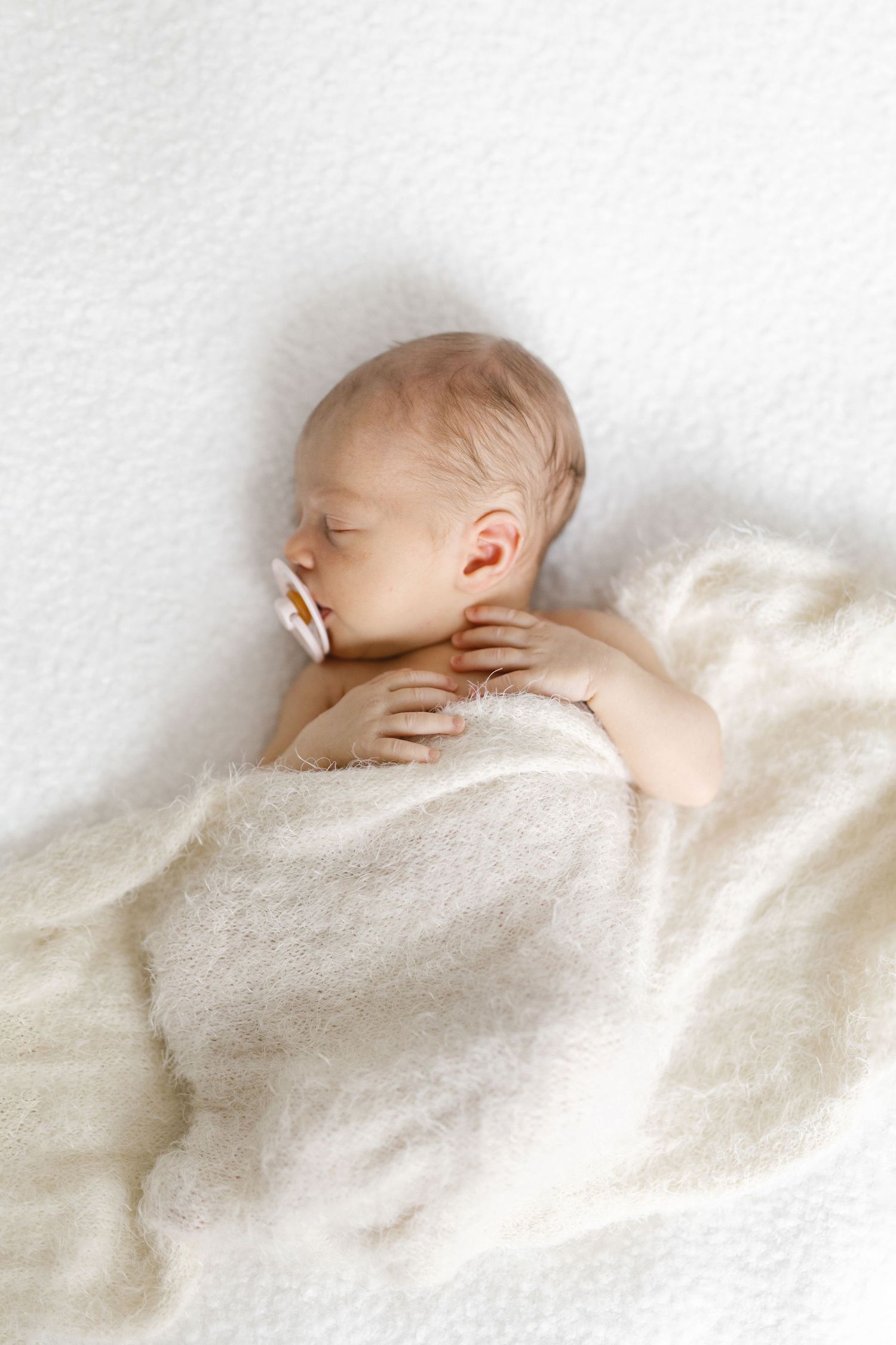 Peaceful sleeping newborn wrapped in soft white blanket against white background.