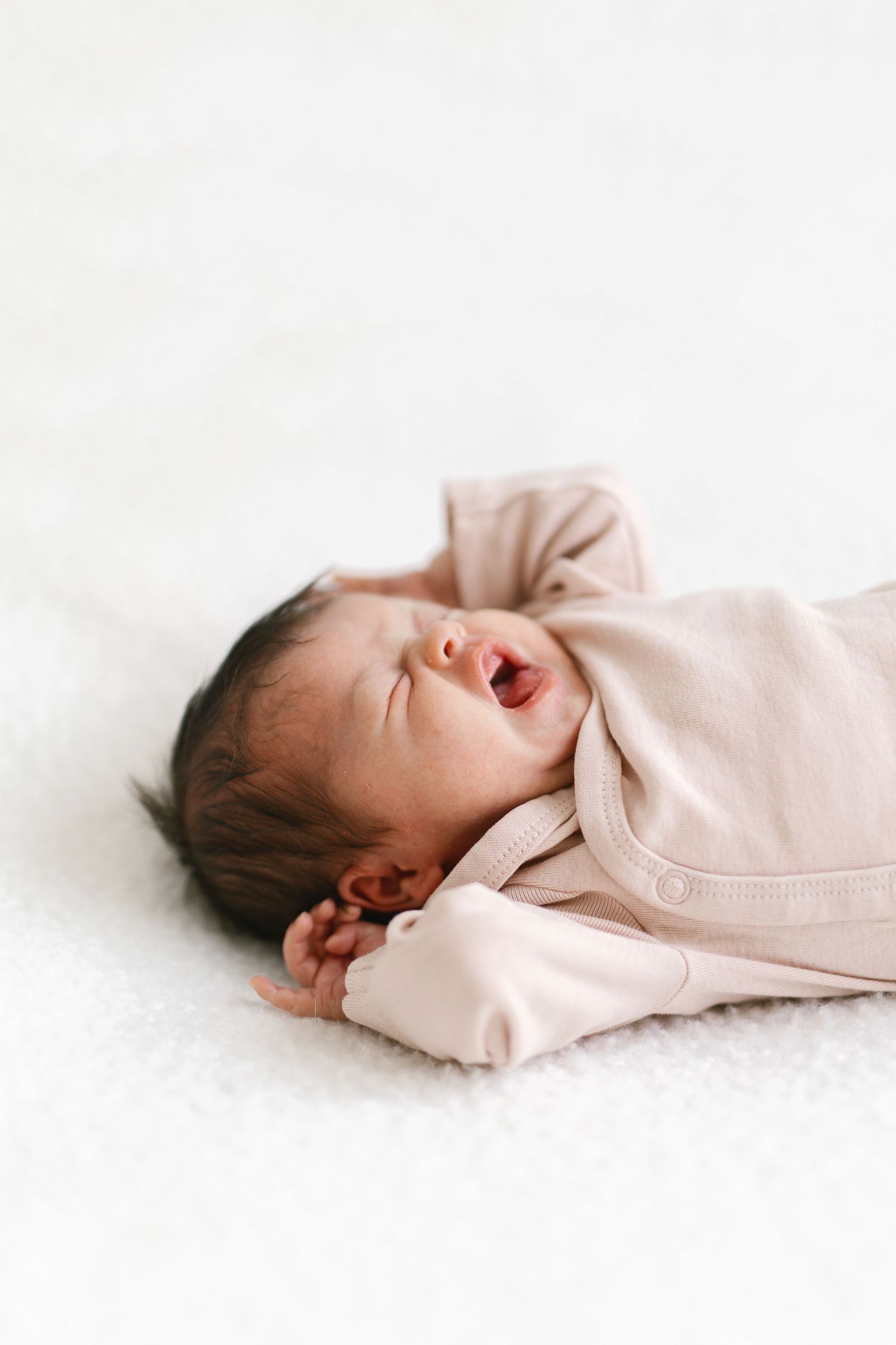 Sleeping newborn in pale pink outfit on white background.