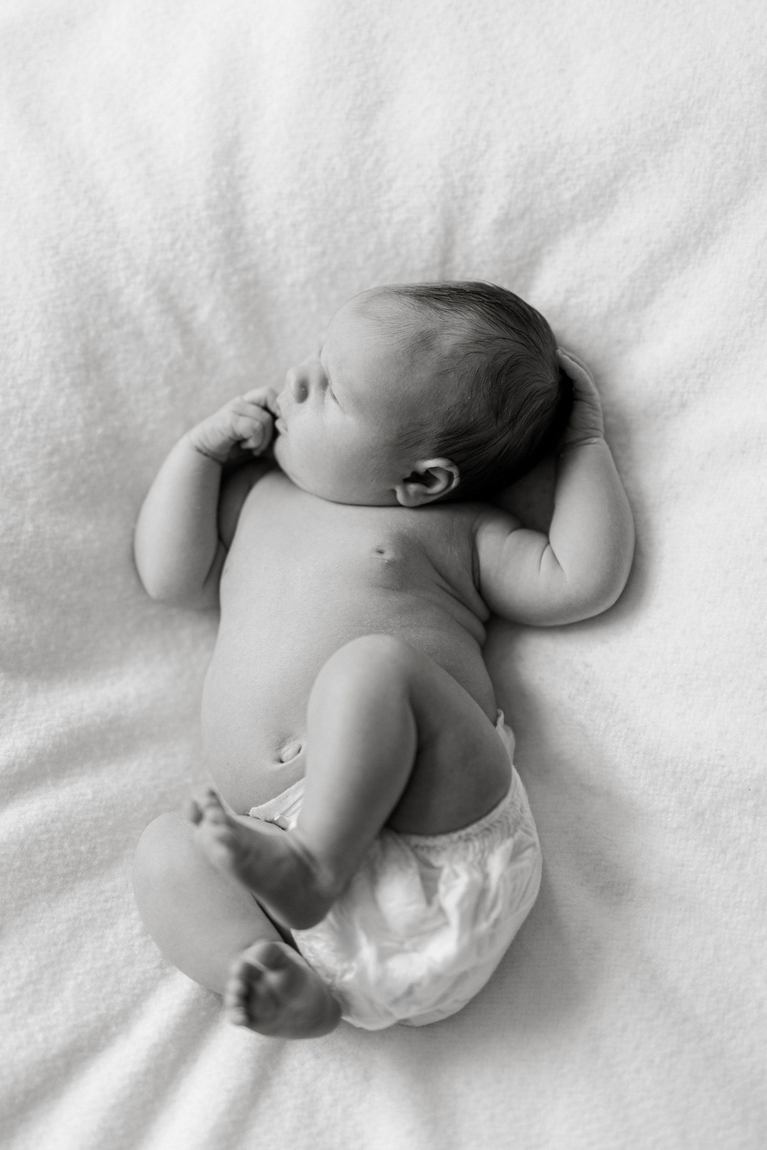 Black and white photo of a peaceful newborn baby lying on a white blanket in a diaper.