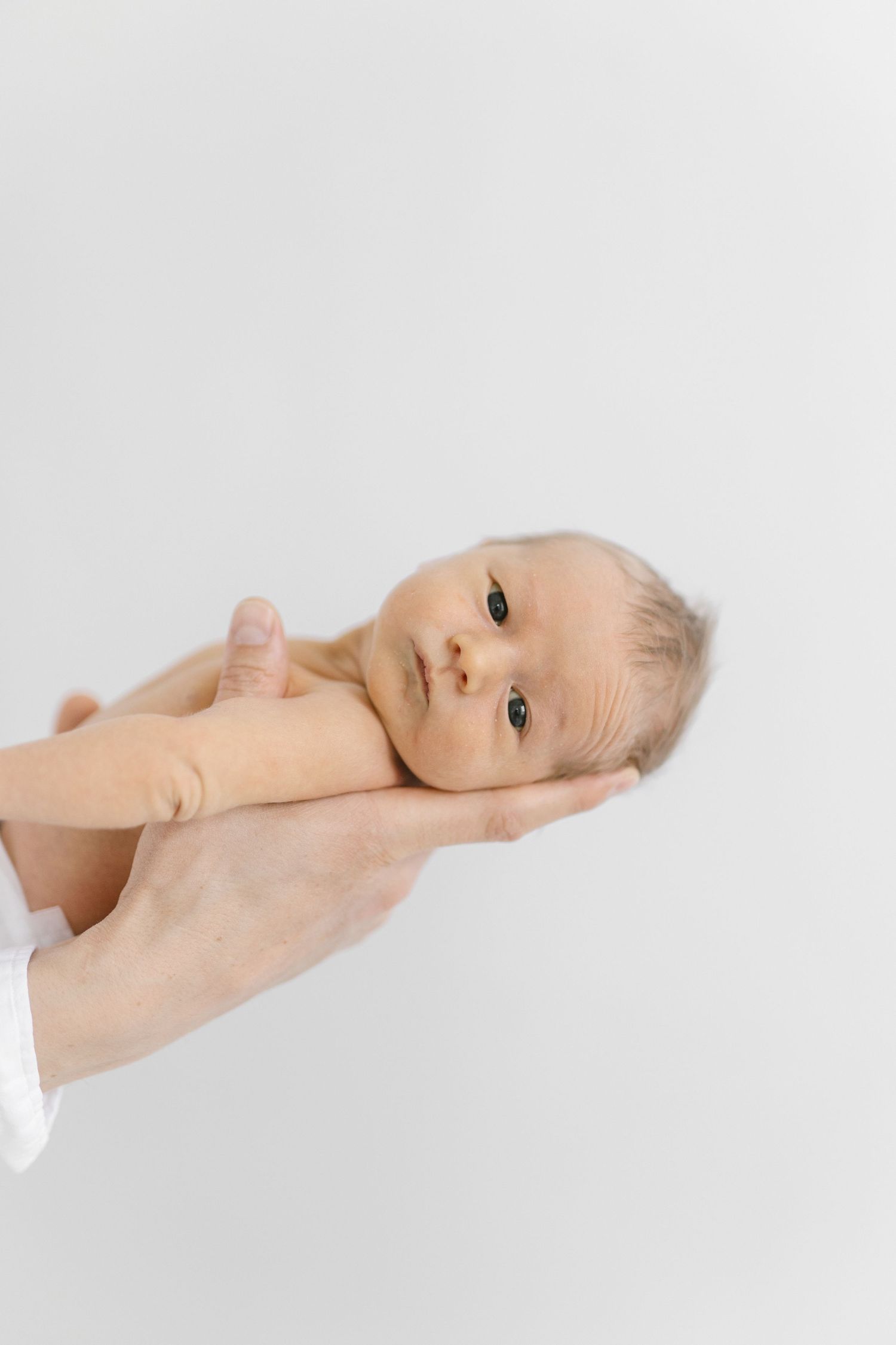 Newborn baby lying peacefully on white background supported by gentle hands.