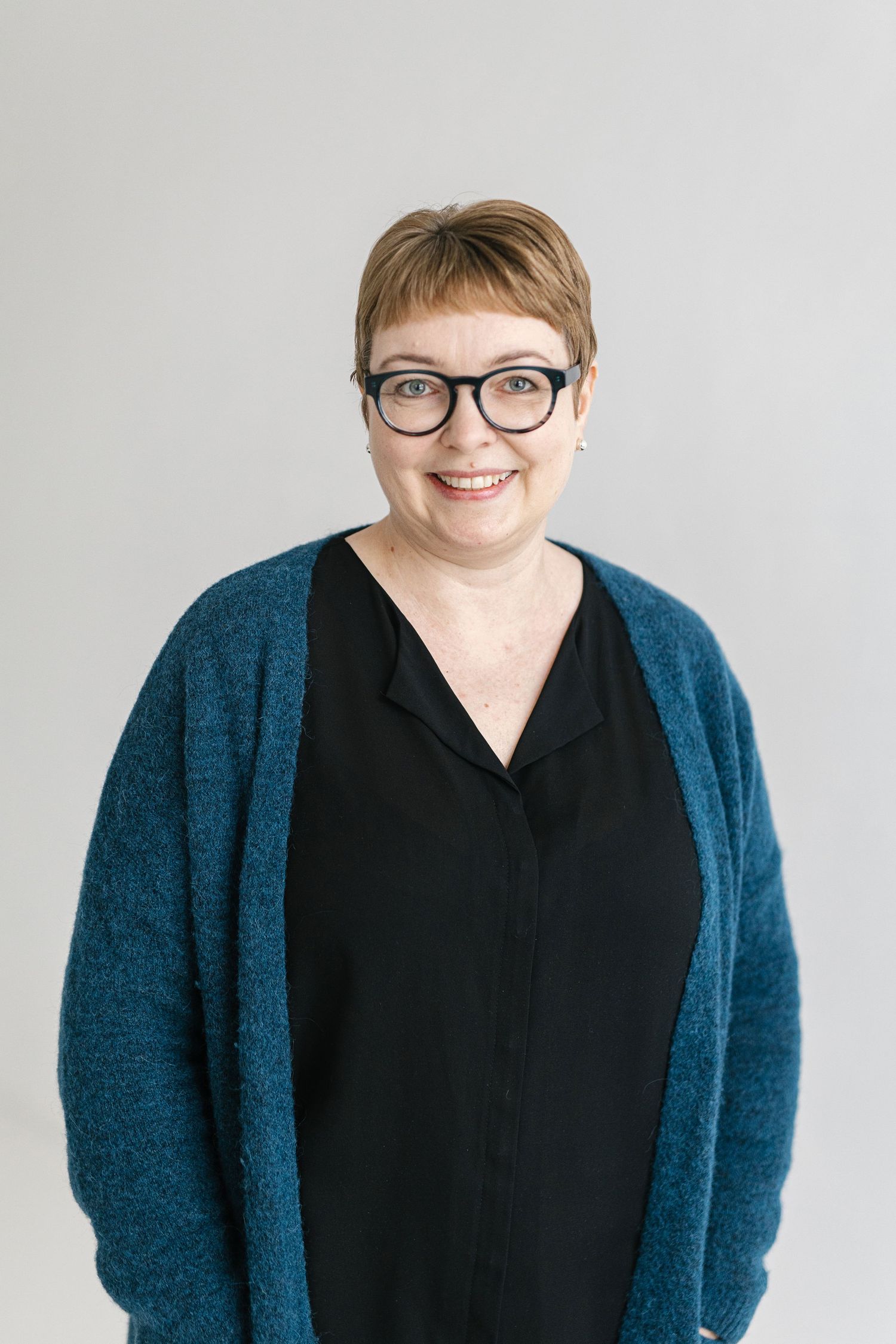 Person wearing glasses and a black top with teal cardigan poses against white background in professional headshot series.