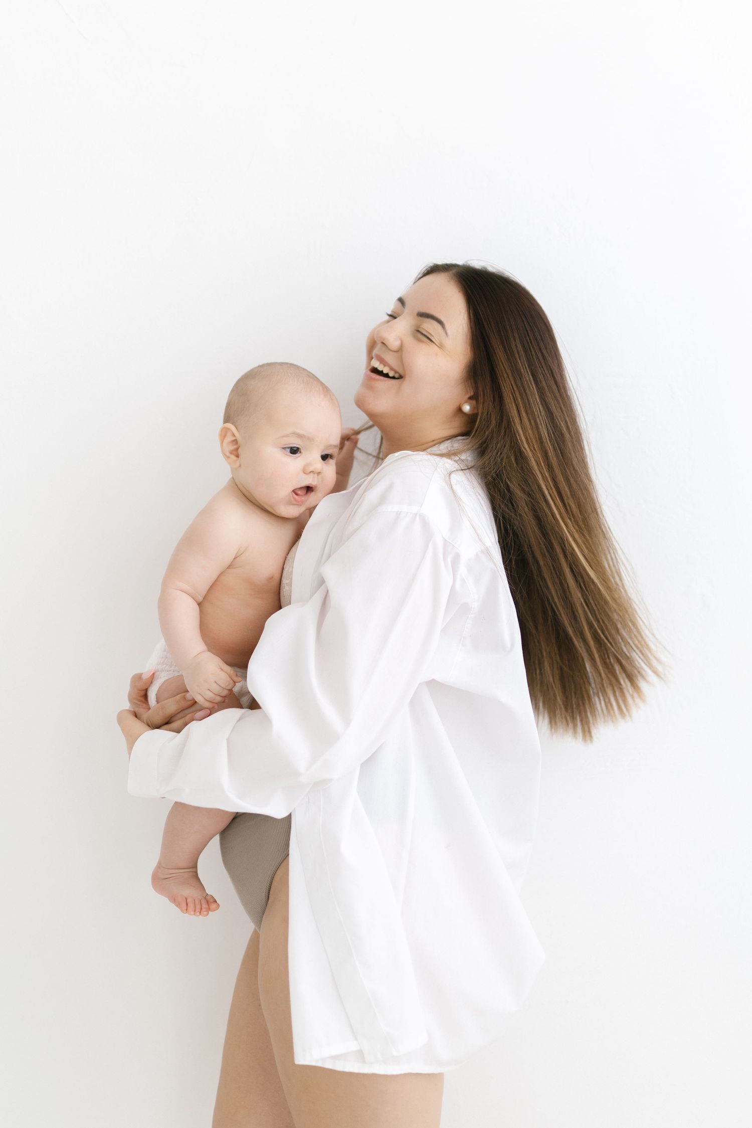 Smiling young mother in white shirt holding her baby against a white background.