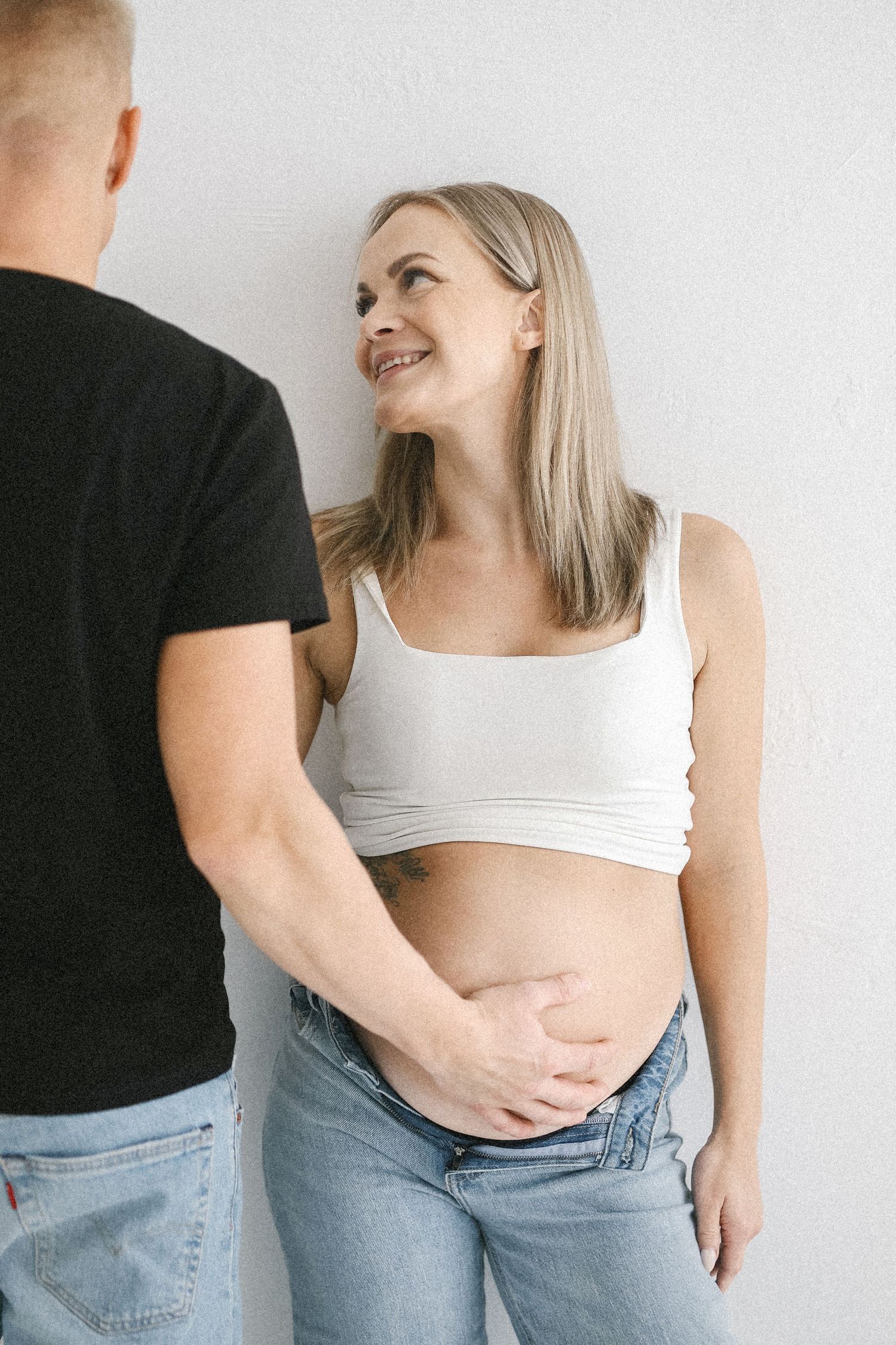 Intimate maternity photos of couple embracing and sharing moments against white backdrop.