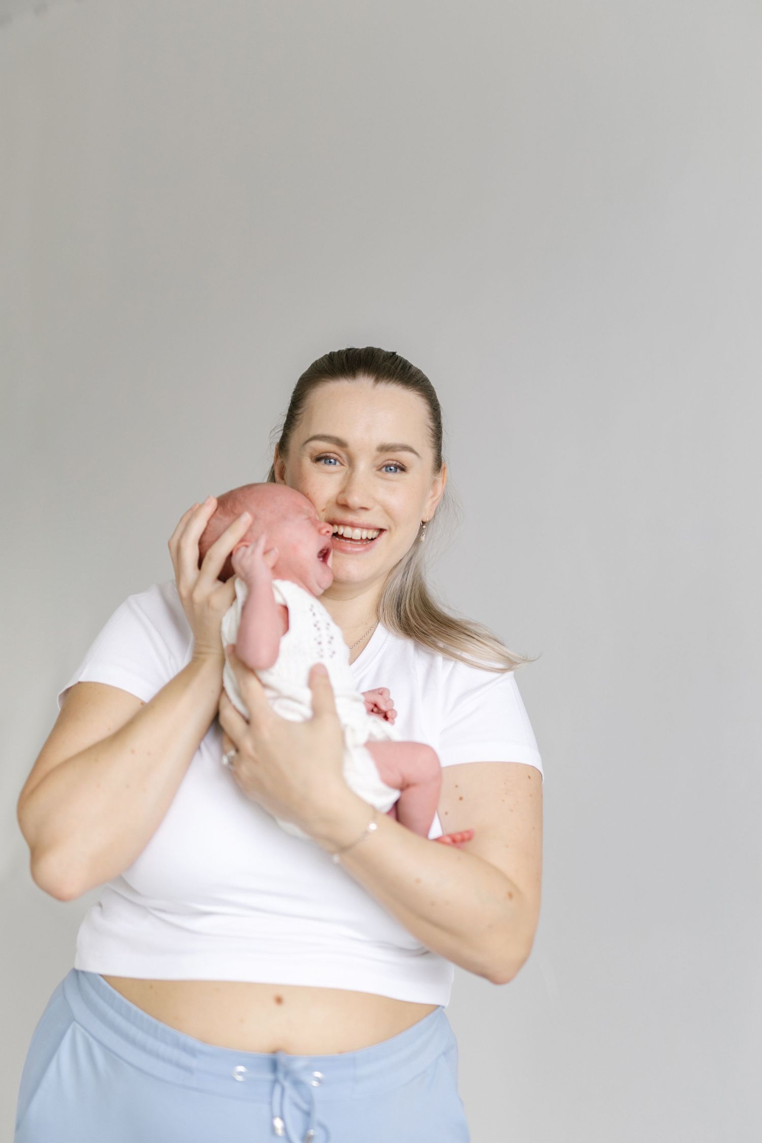 Person in white shirt and blue pants playfully holding pink baby clothing.