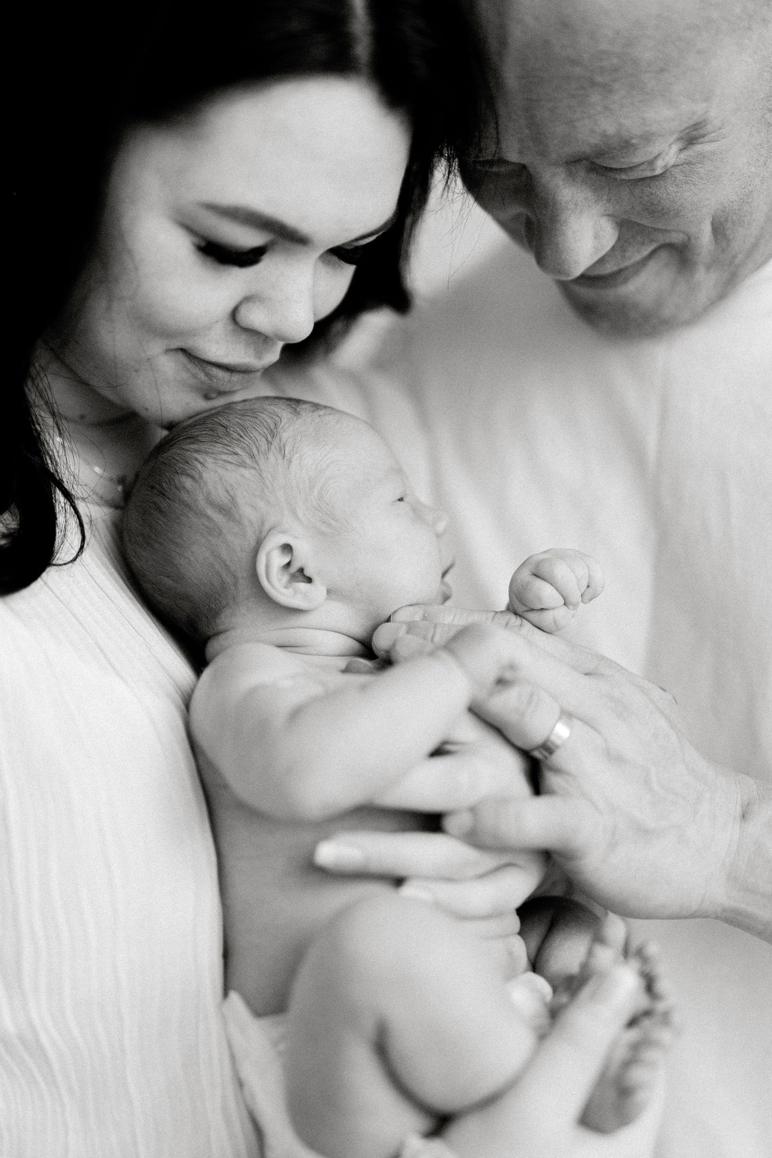 A tender black and white portrait of parents cradling their newborn baby with gentle expressions of love.