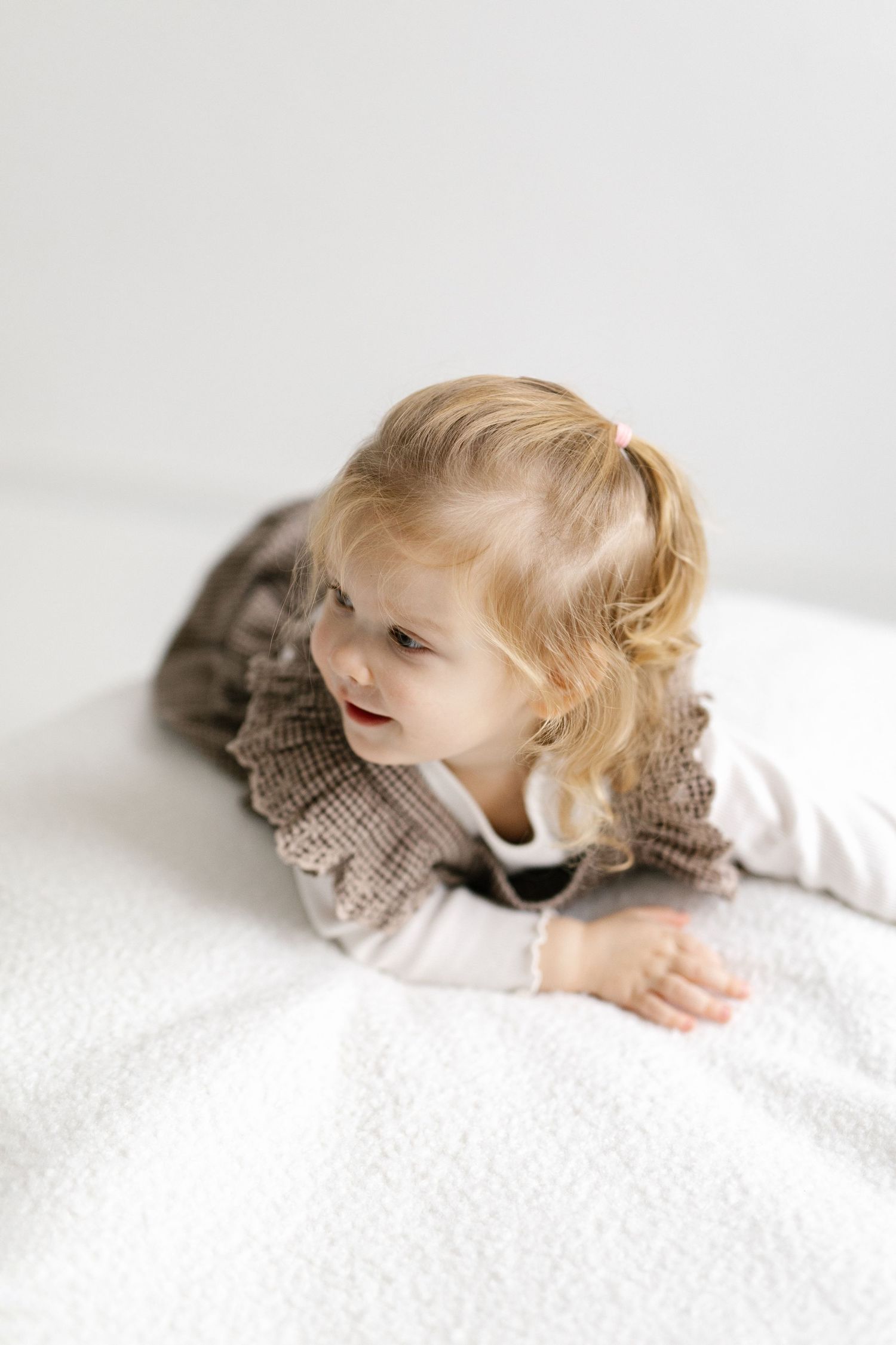 Child in white clothing lying down on textured white surface.