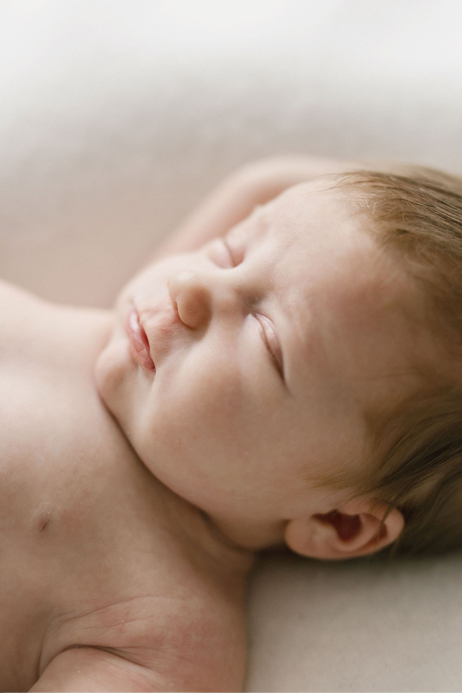 A peaceful newborn baby sleeping soundly with eyes closed, soft skin glowing in gentle natural light.