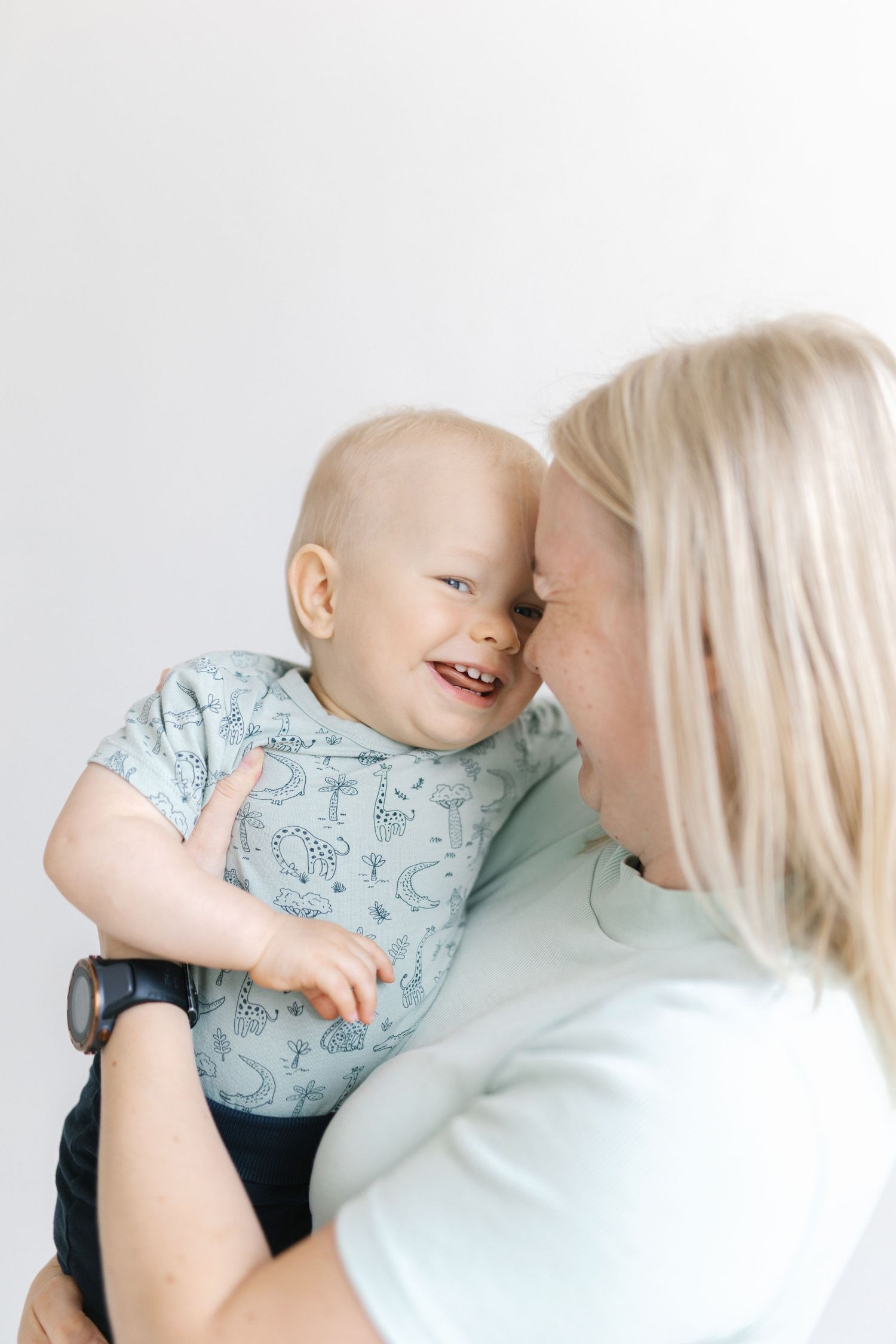 A tender moment captured between a baby in a patterned shirt and caregiver against a white backdrop.