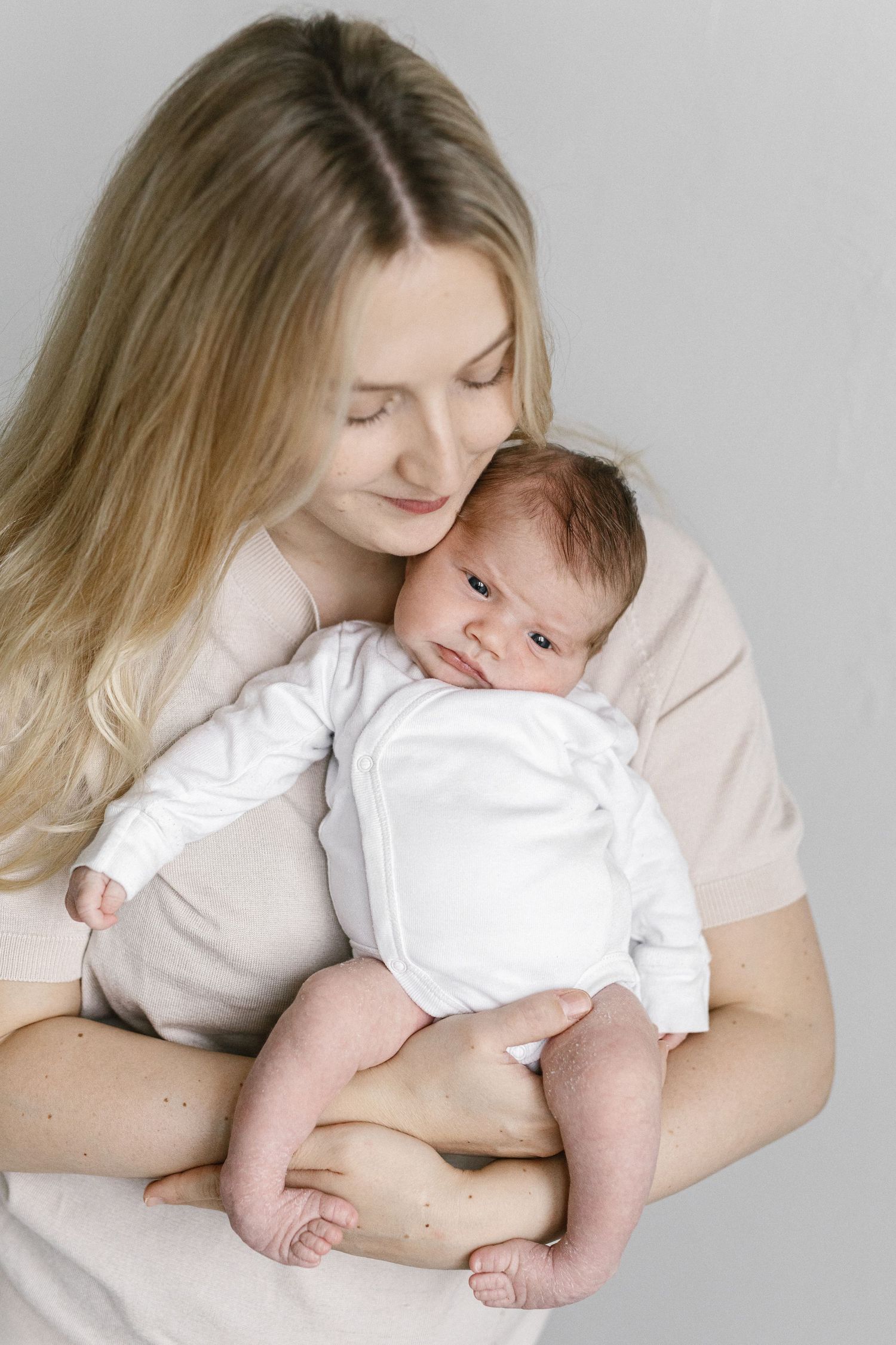 Gentle portrait series of parent holding and cuddling infant in white clothing.
