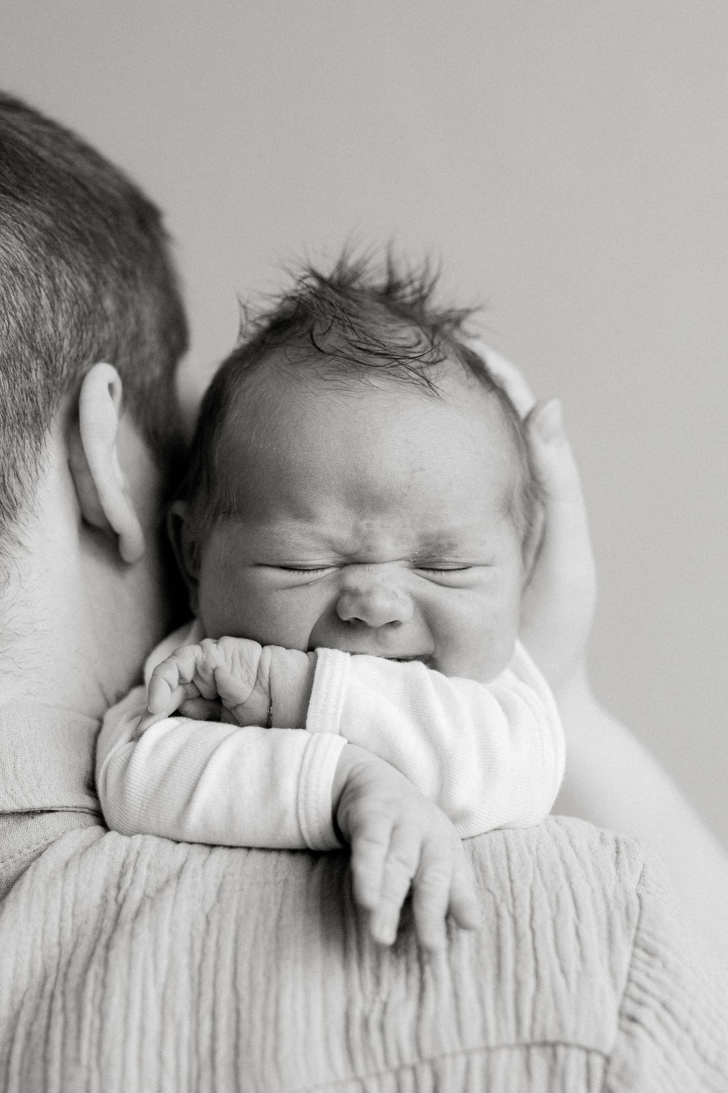 Close-up of newborn with spiky hair resting on adult's shoulder.