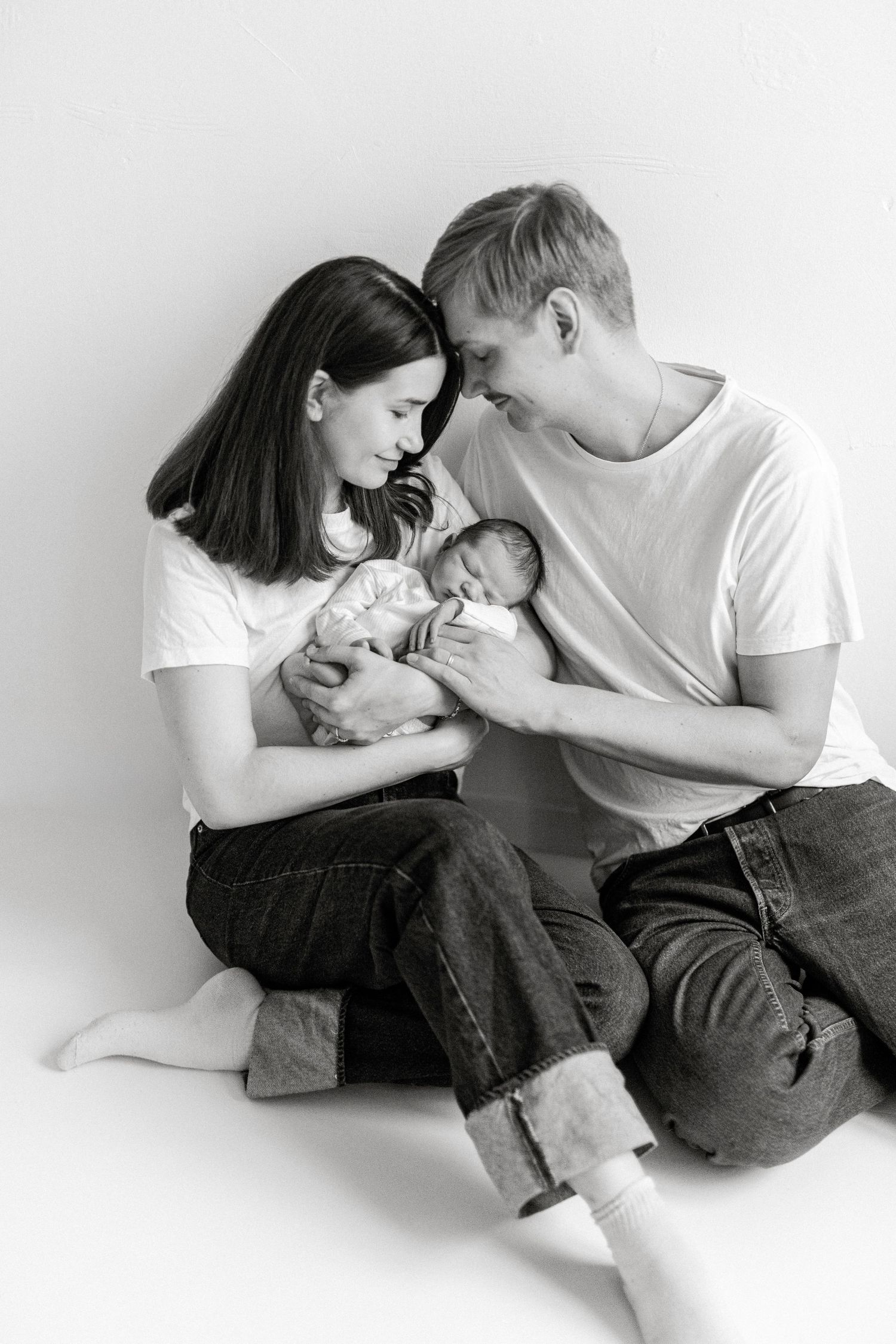 A couple in casual clothing sharing an intimate moment while sitting together against a white background.