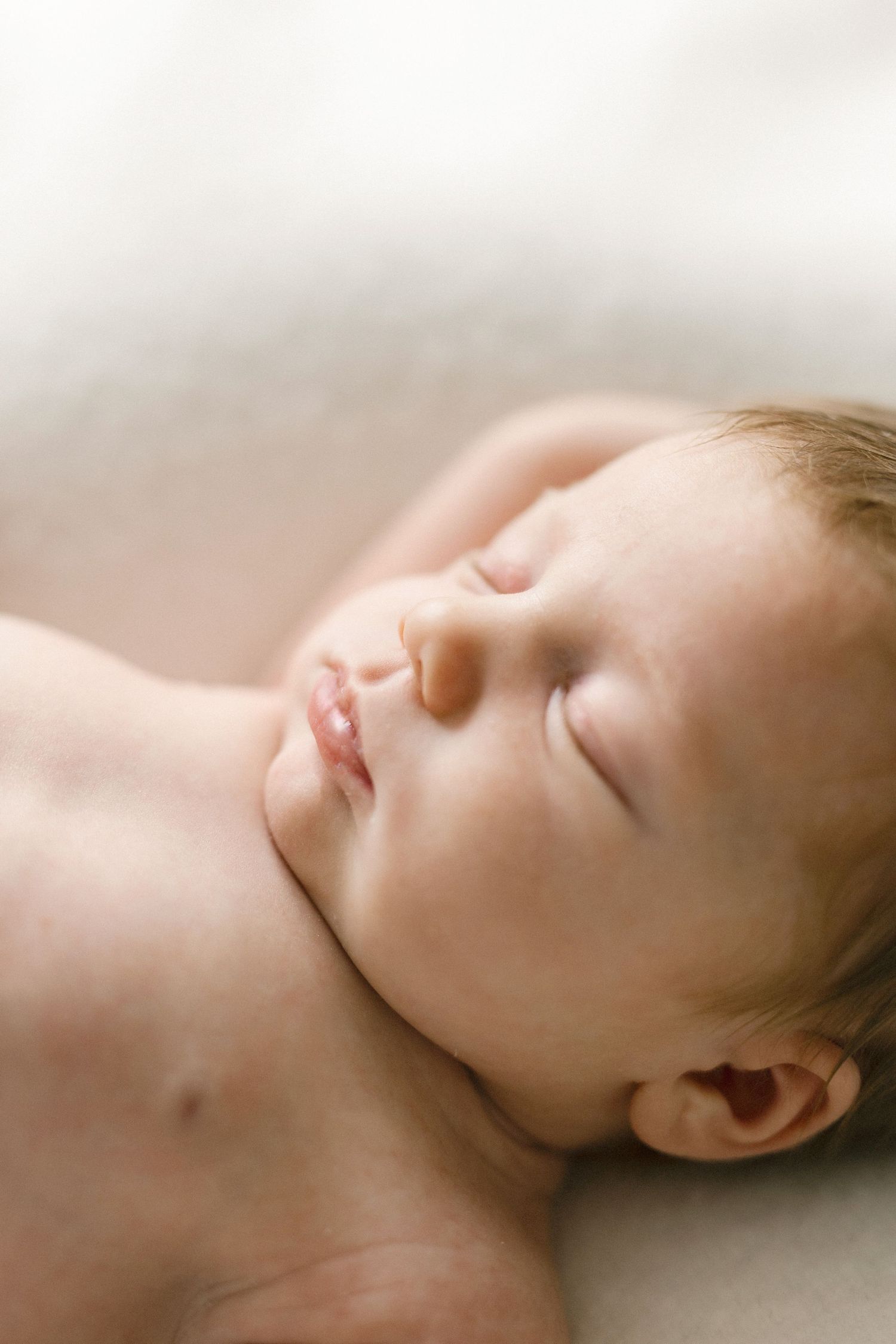 Peaceful newborn baby sleeping on a soft white blanket, with delicate features and light hair.