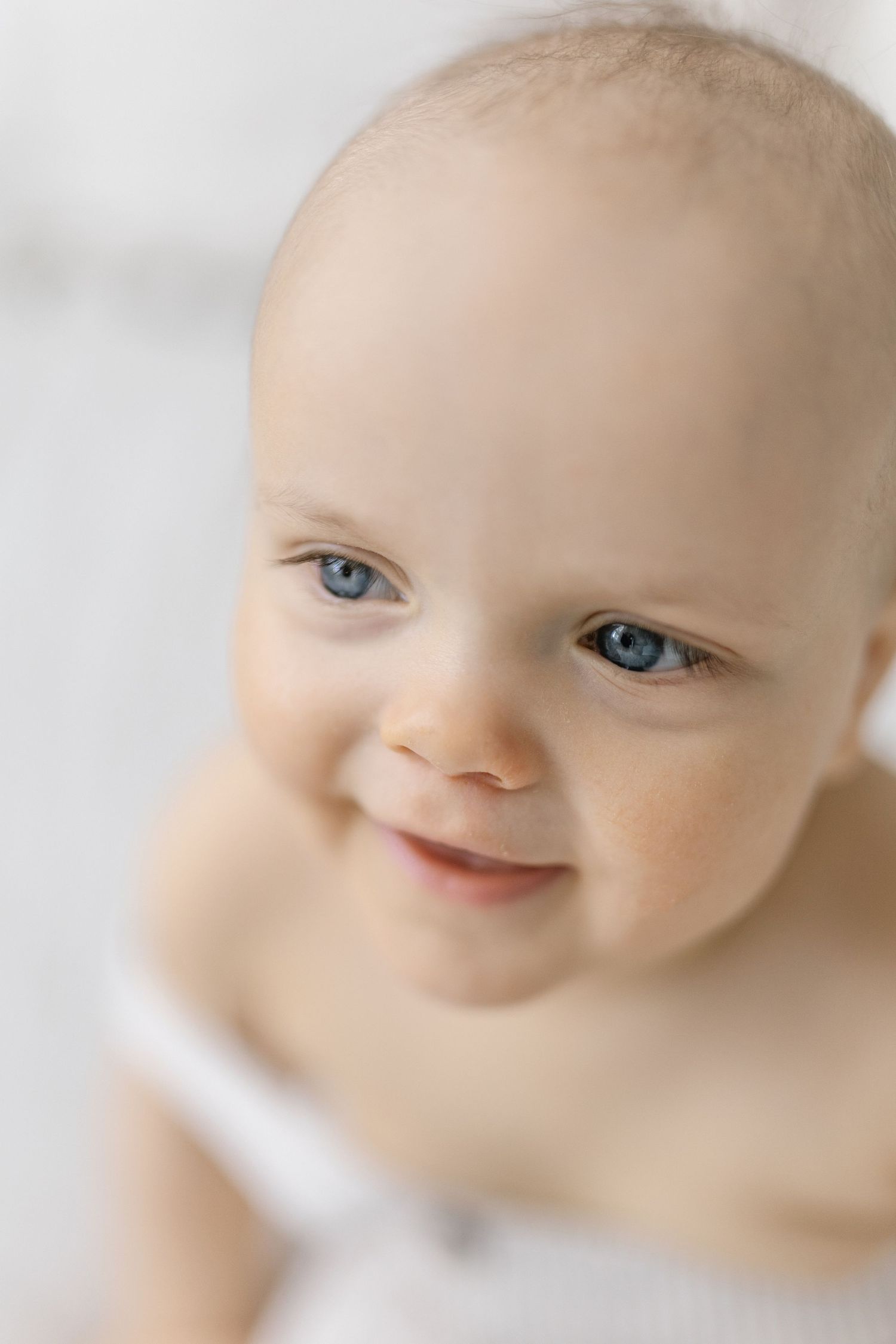 Adorable baby with blue eyes and a sweet smile, with fair skin and light hair, looking up at the camera.
