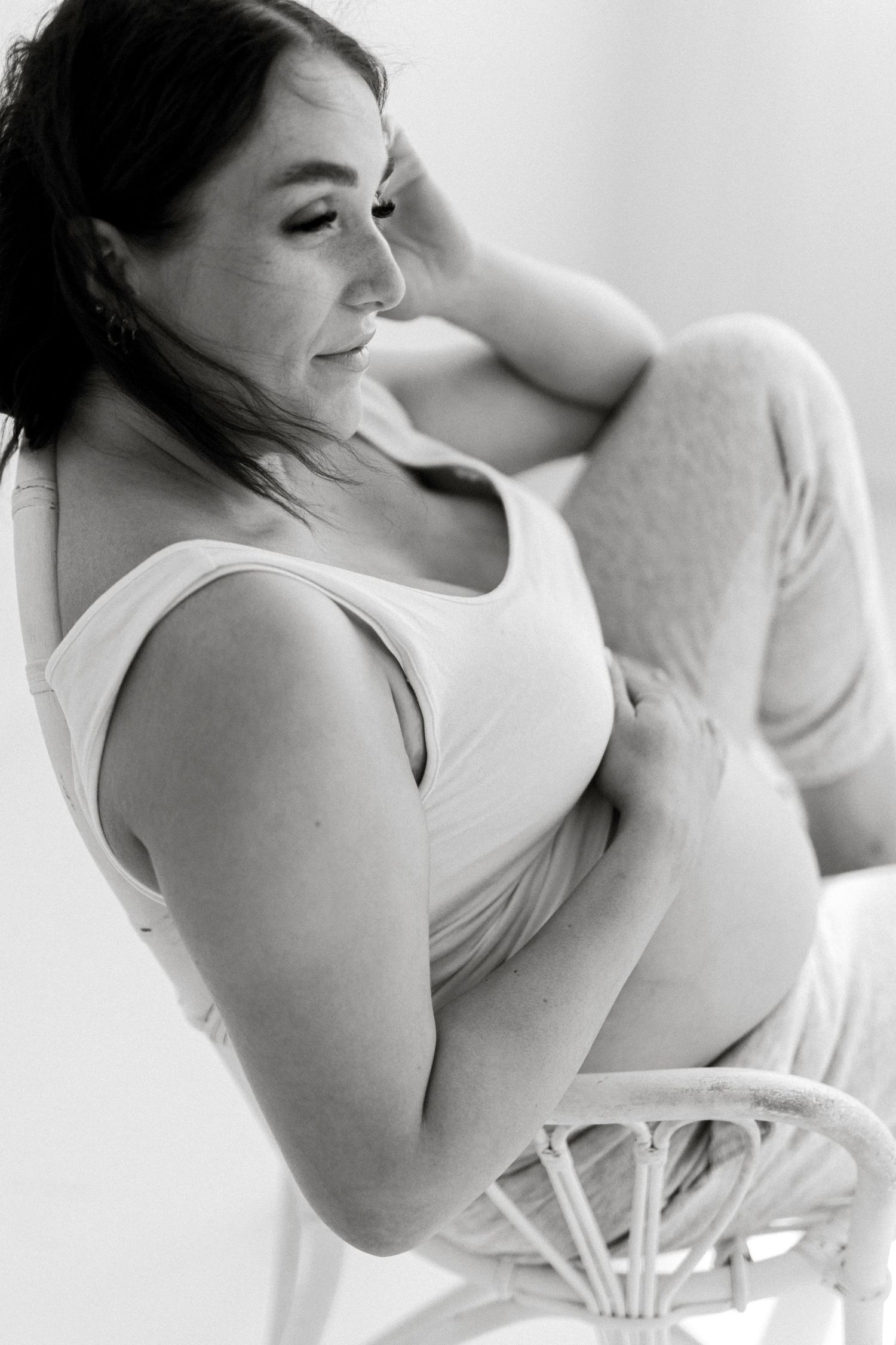 Black and white portrait of woman in white tank top sitting in casual pose.