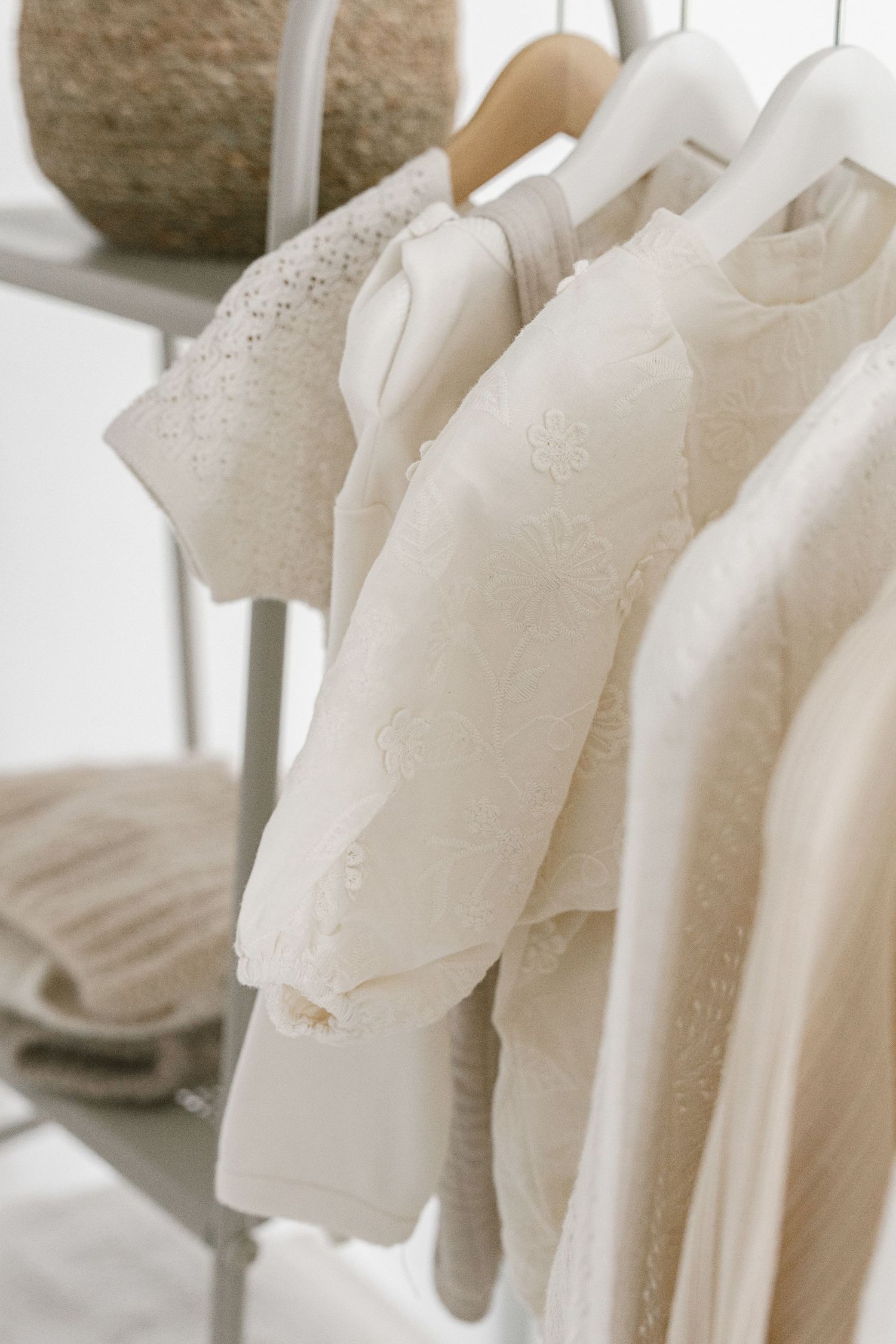 Elegant cream and white lace blouses hanging on a clothing rack with wooden hangers in a bright, minimalist setting.