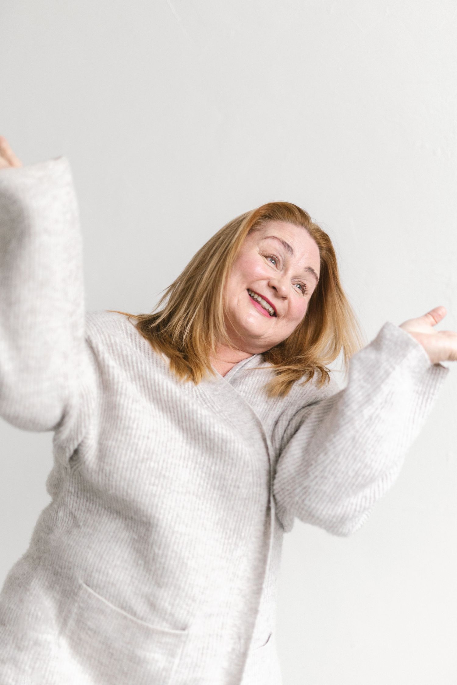Someone wearing a cozy white sweater jumps joyfully against a light background while expressing happiness.