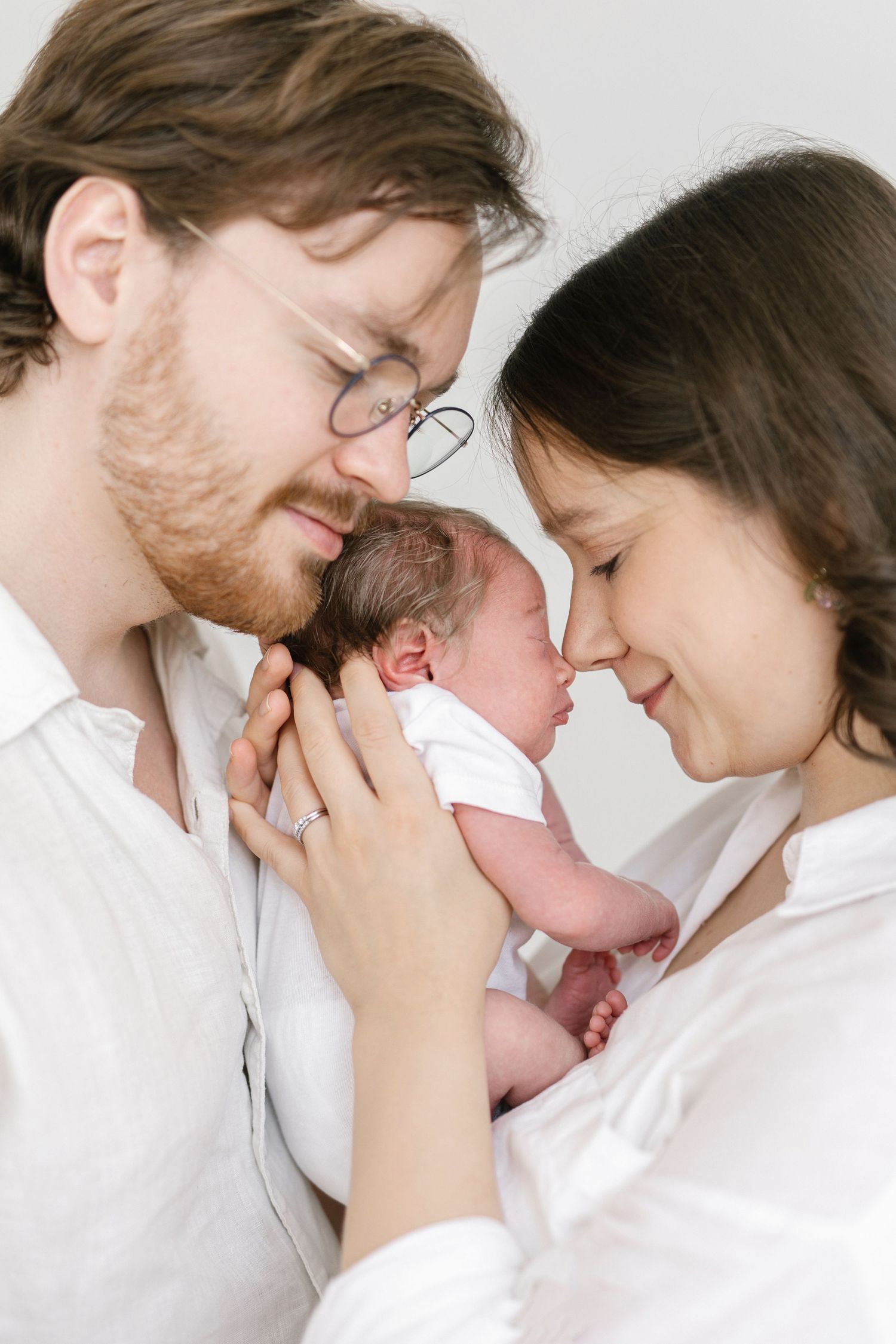 New parents tenderly hold their newborn baby close, touching foreheads in an intimate family portrait.