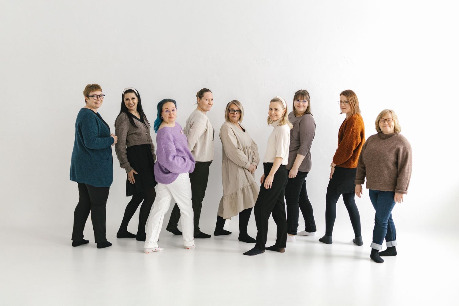 Group of nine women posing together in casual outfits against a white background in a professional photo shoot.