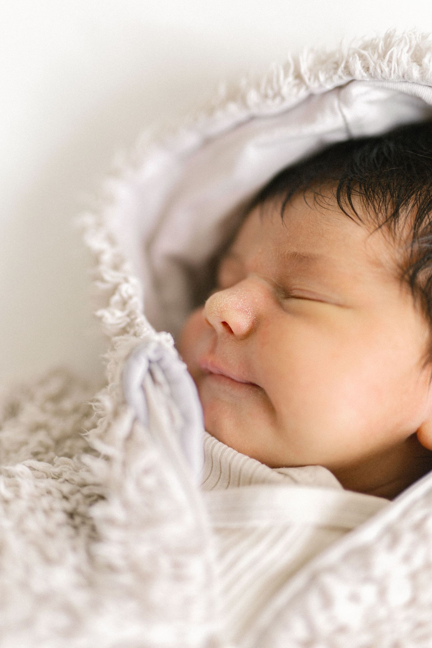 A peaceful newborn baby sleeping soundly, swaddled in a soft white blanket with dark hair visible.
