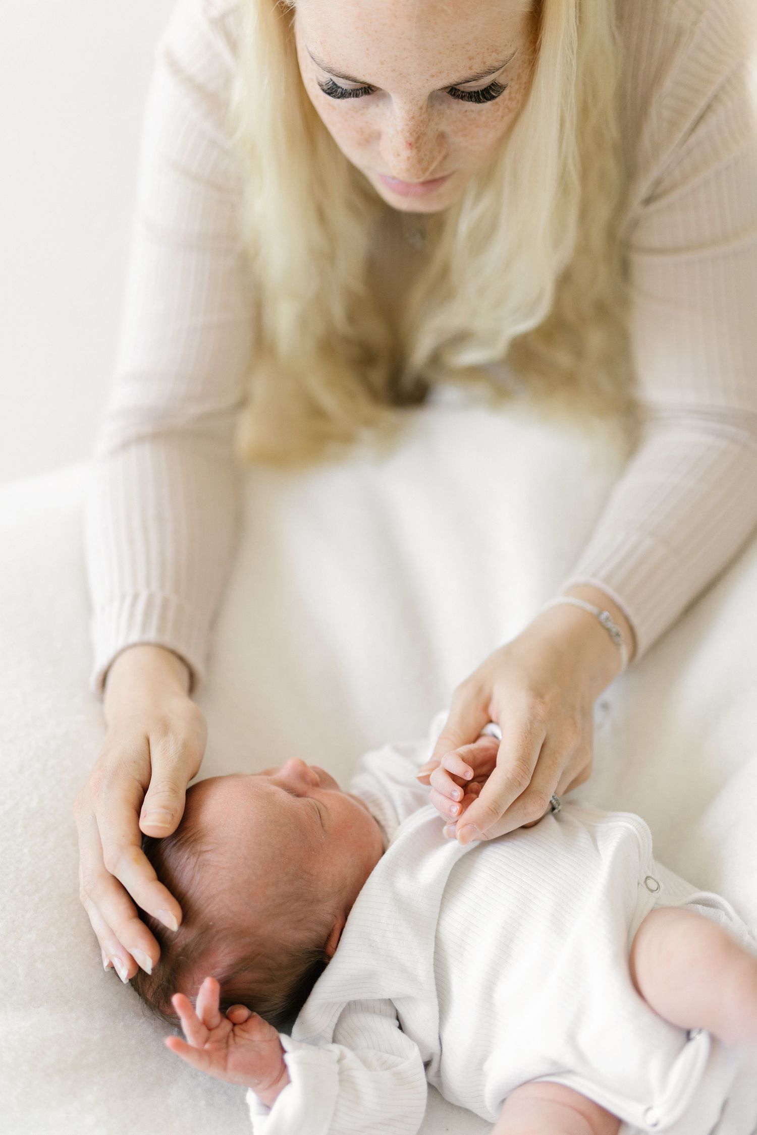 Blonde mother tenderly cradling her newborn baby in white, sharing a gentle moment of connection.