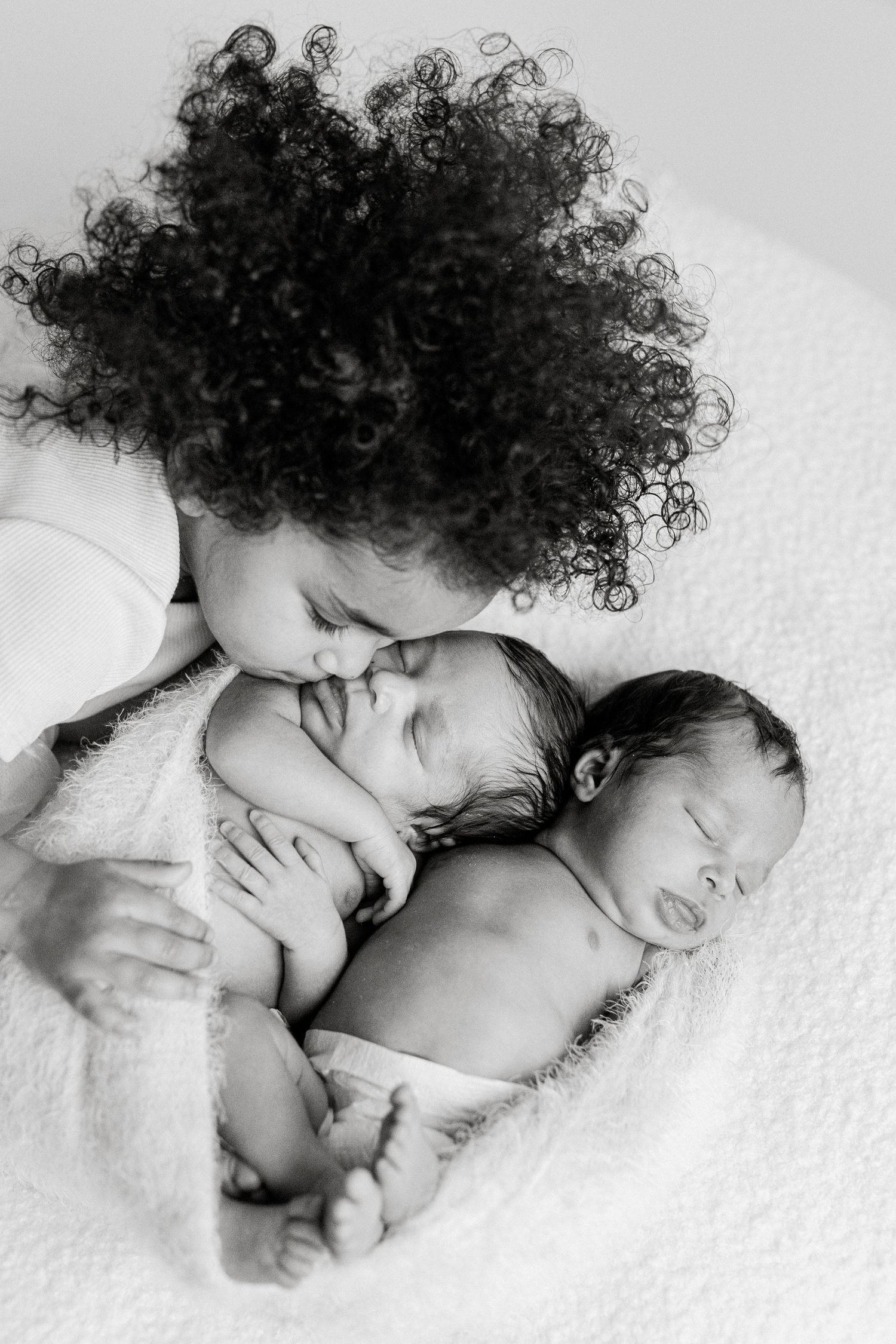 Black and white portraits showing tender sibling moments with a newborn baby.
