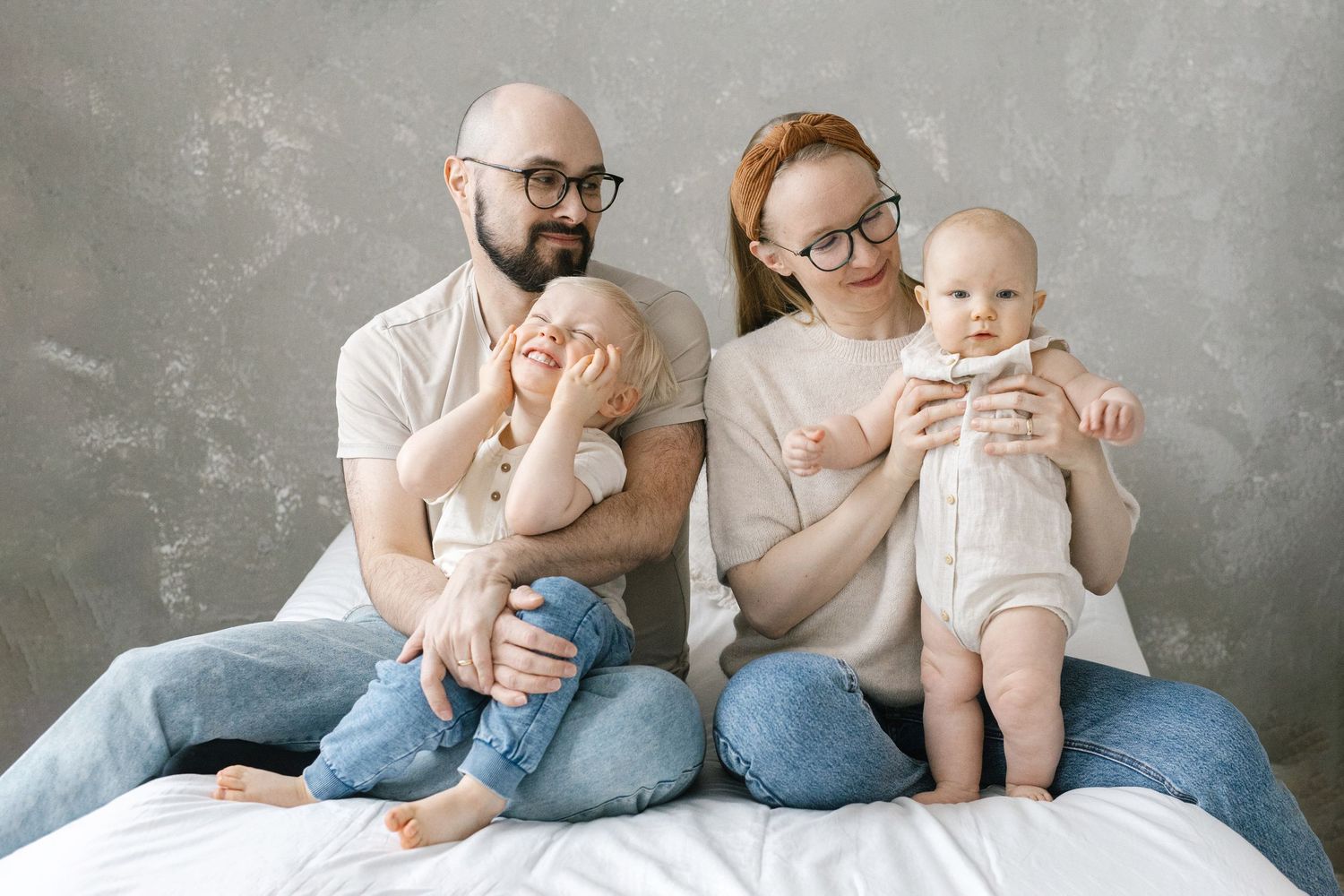 Family portrait of parents with young children sitting together on bed.