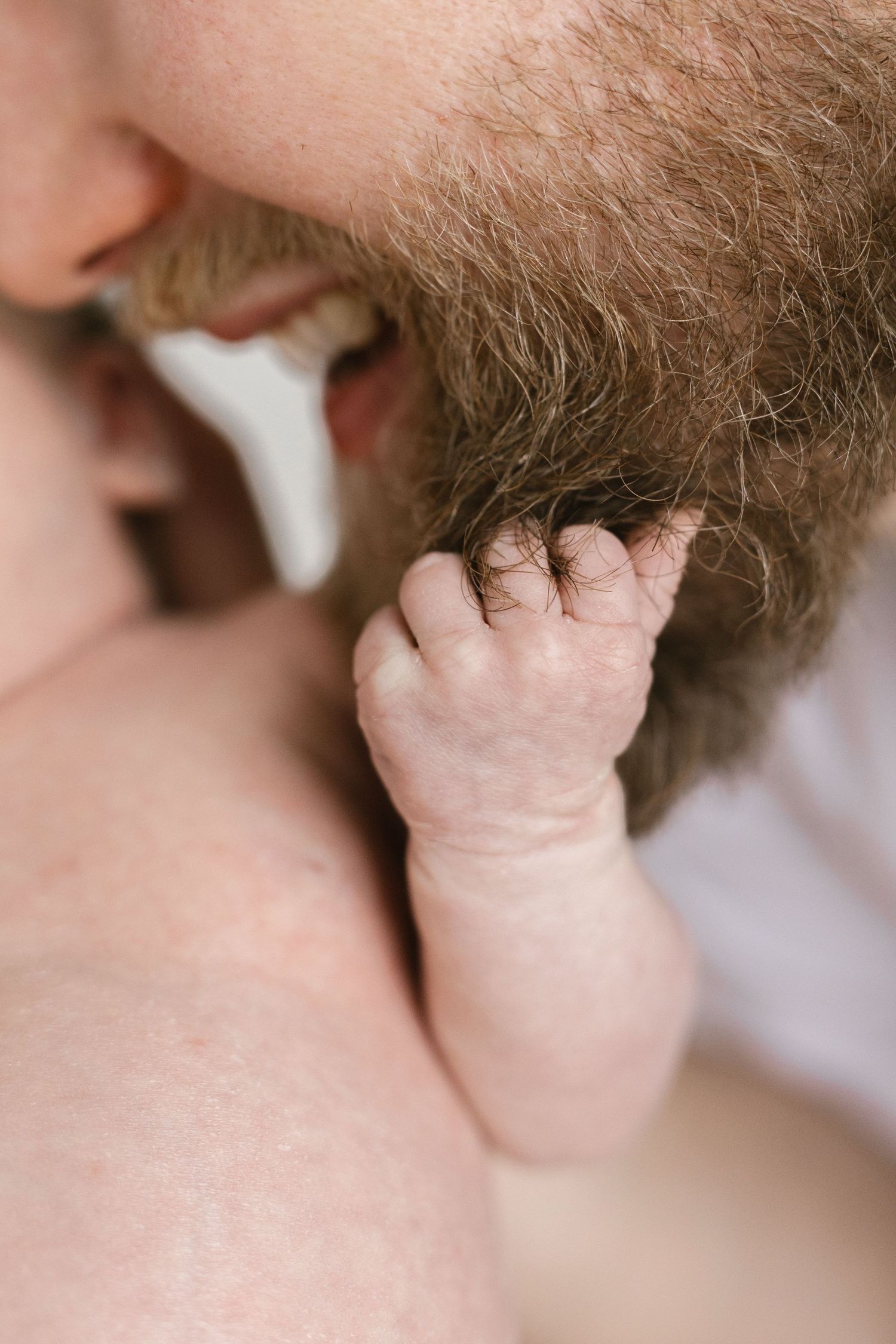 Close-up of tiny baby hand touching parent's facial hair.