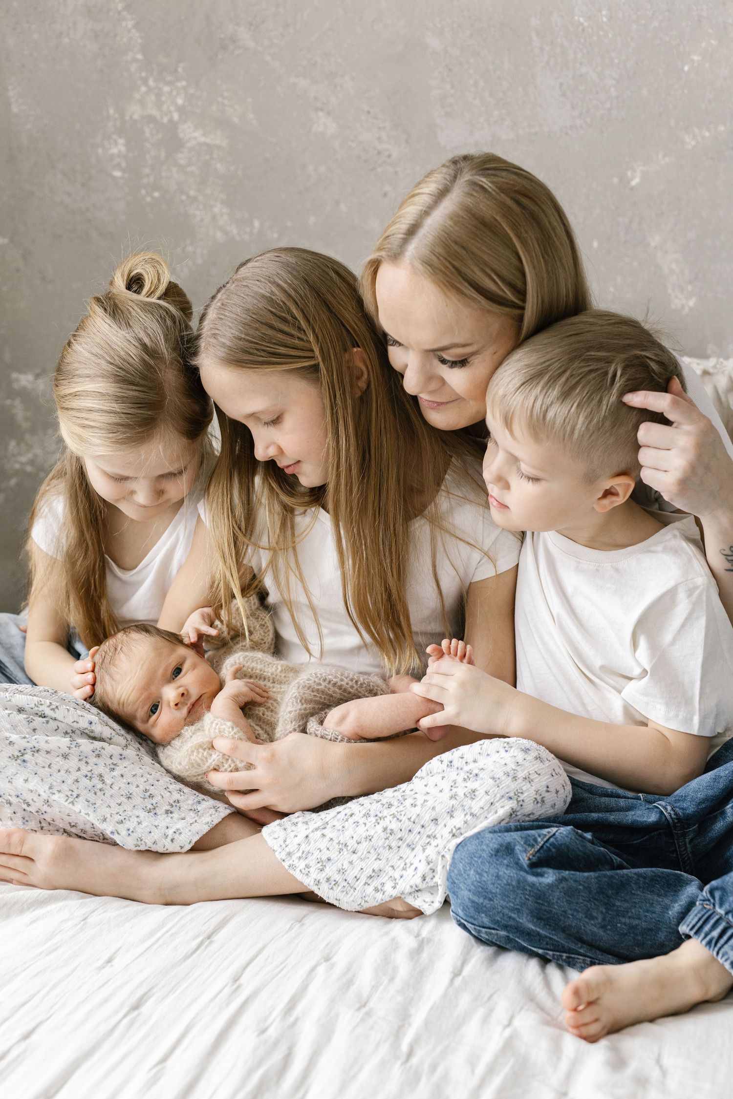 A mother with three children and a newborn baby sitting together on a bed, sharing a tender family moment.