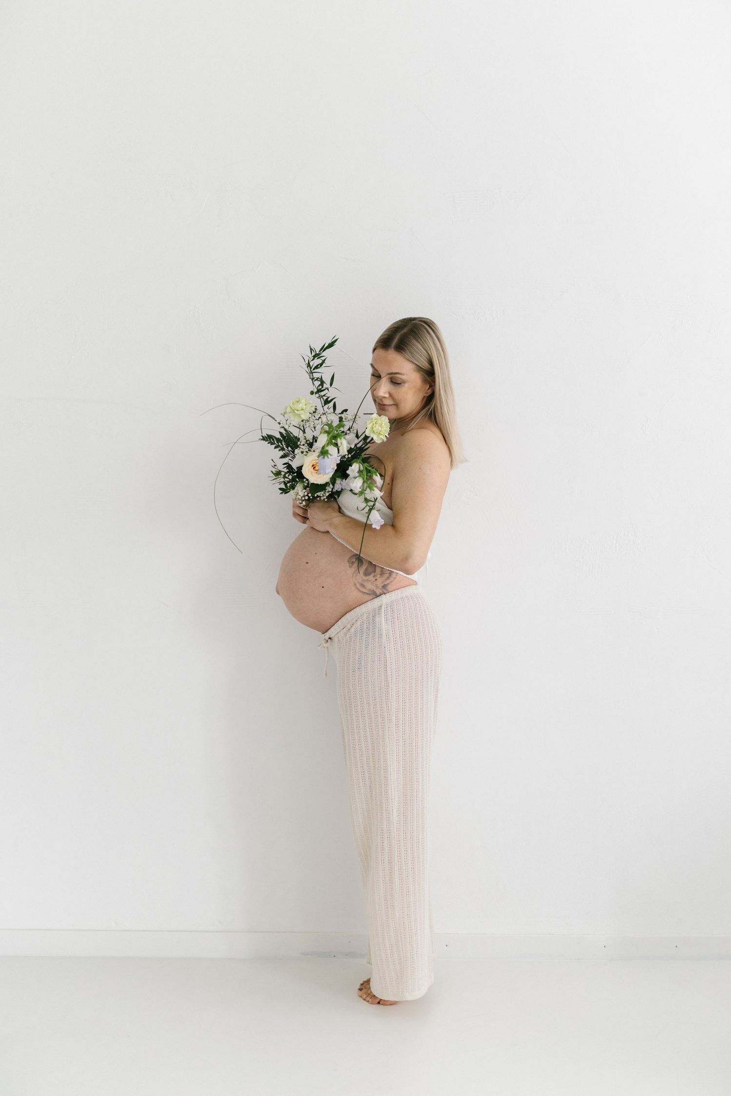 Maternity portrait with woman in cream ribbed dress holding white and green floral bouquet.
