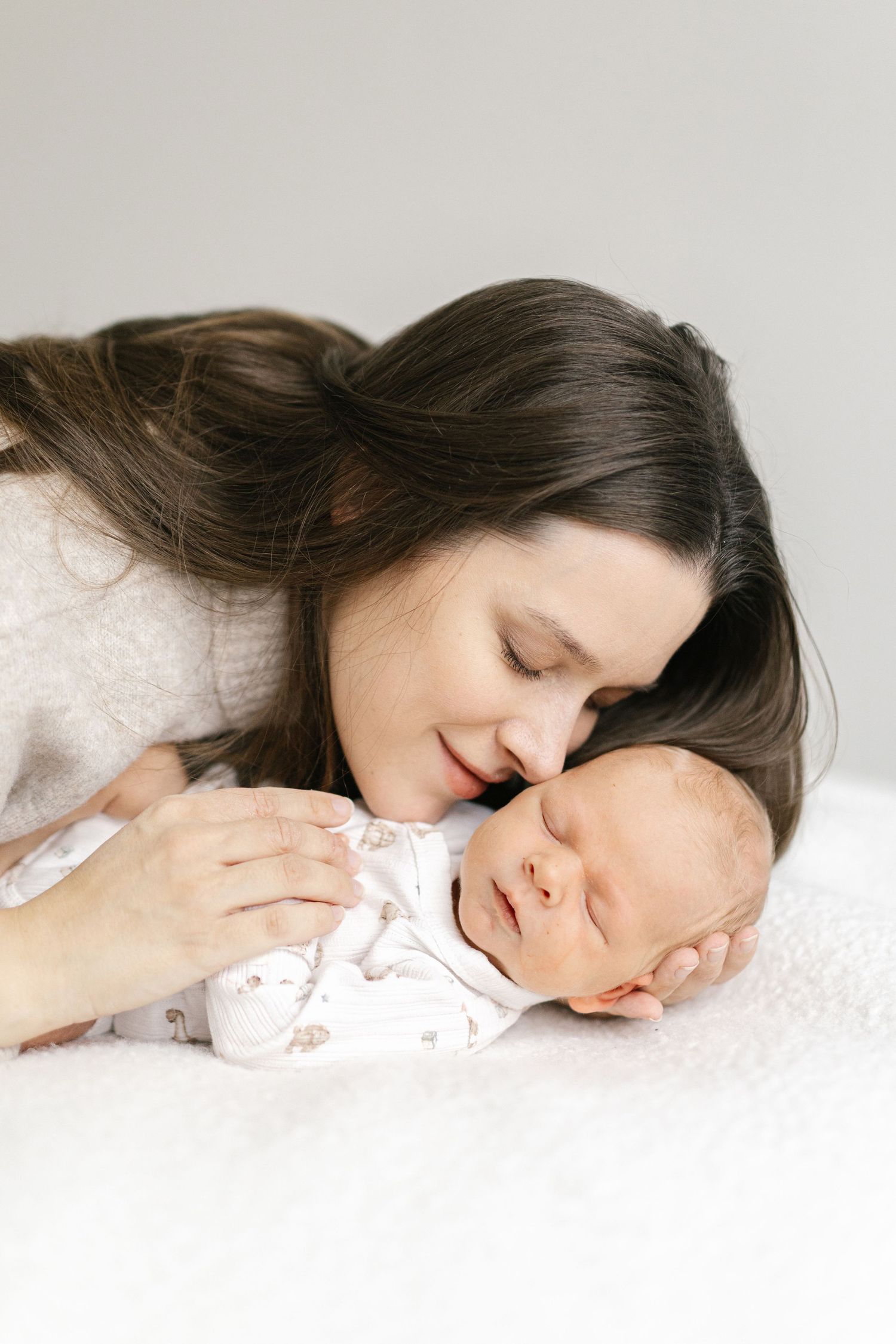 Mother lying on white surface tenderly kissing sleeping baby in sequence.