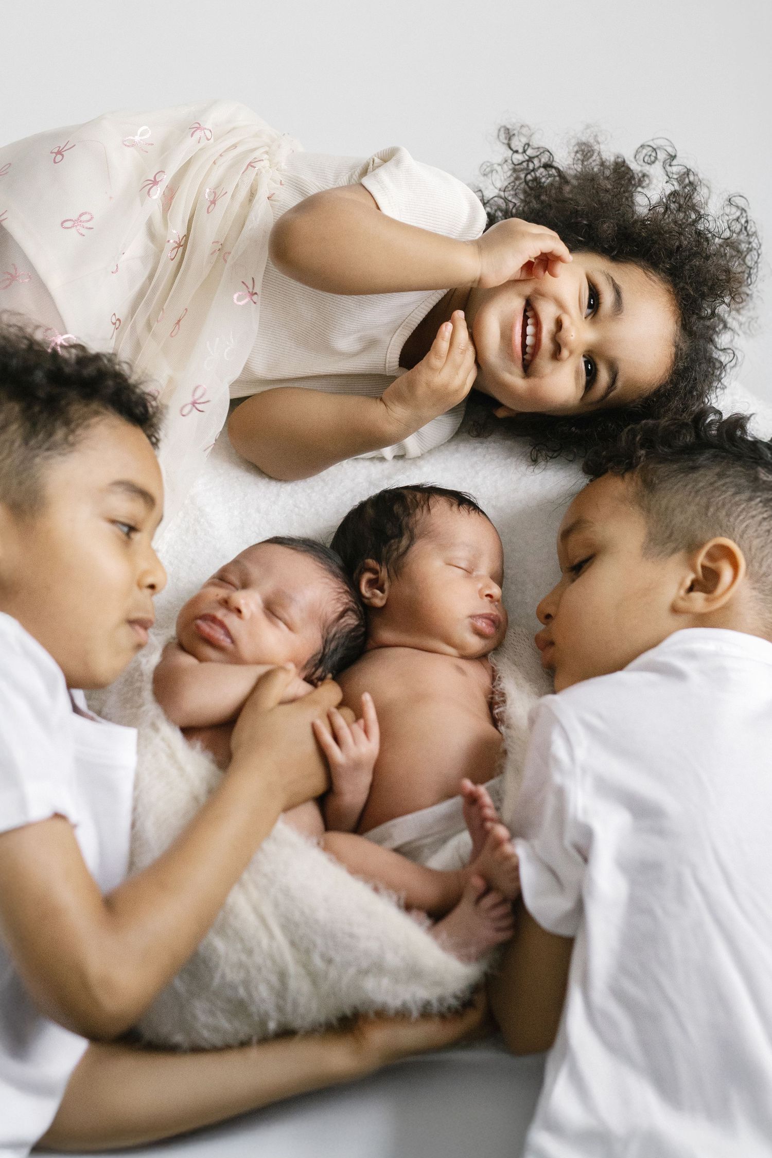 Sweet family moment captured of siblings cuddling with newborn on white bedding.