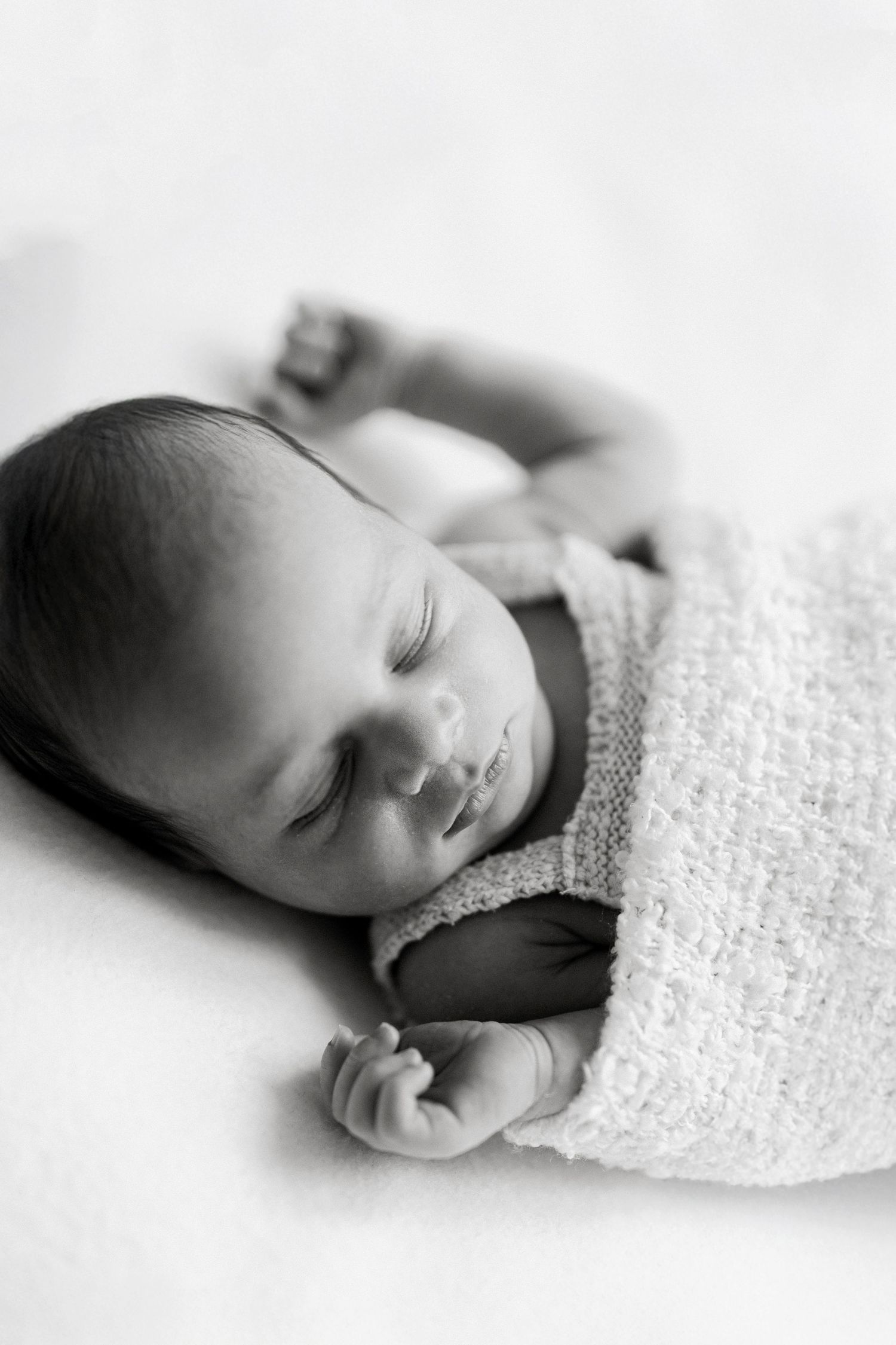 Peaceful black and white portrait of sleeping newborn baby wrapped in soft textured blanket.