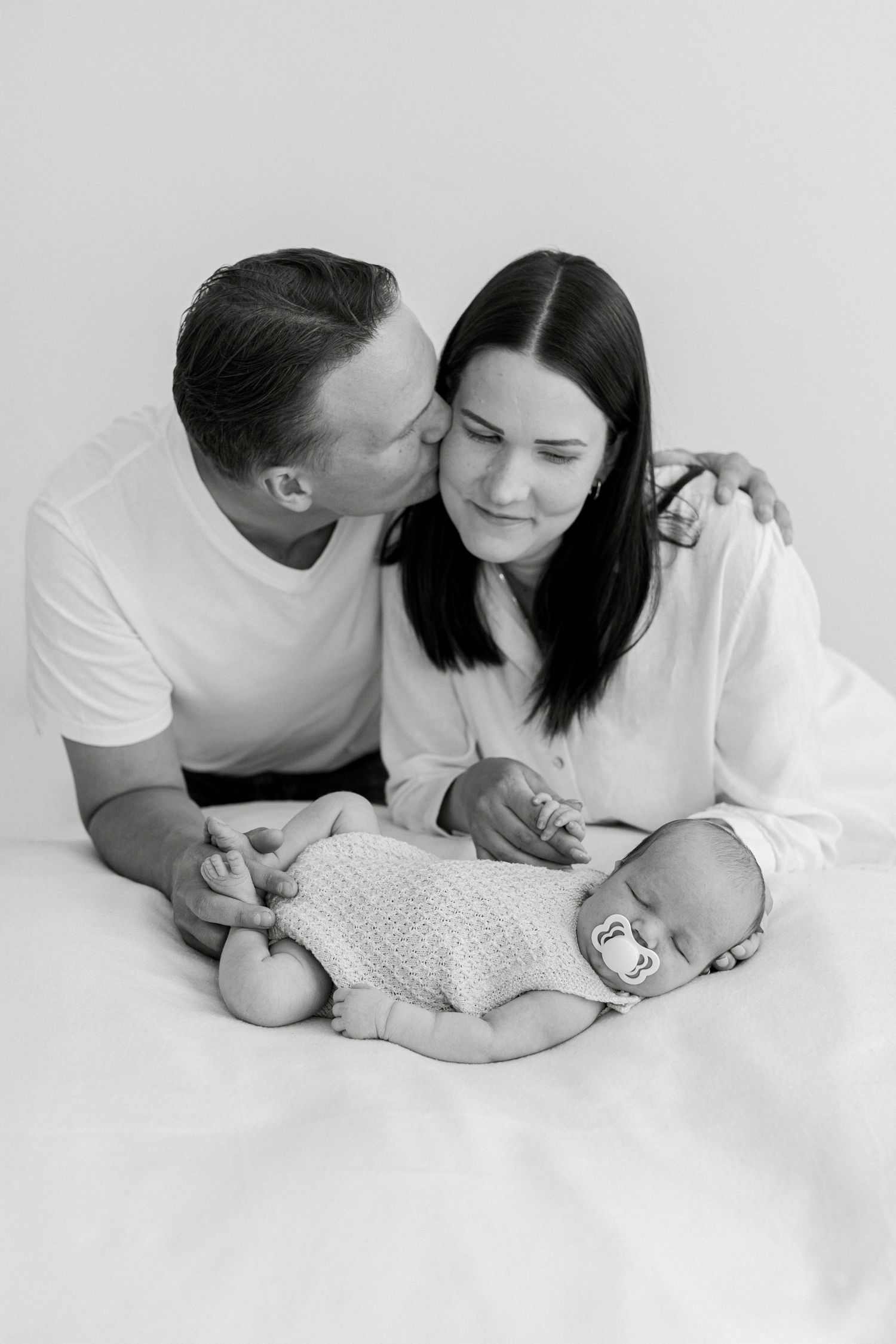 Parents lovingly gazing at their newborn baby on white bedding in black and white photography.