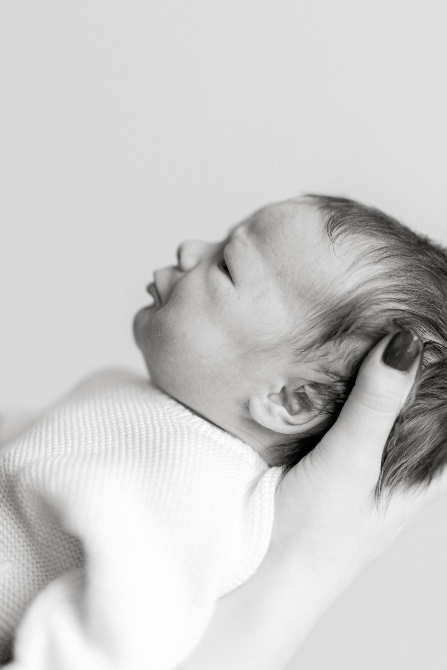 Side profile of baby in white clothing lying on textured surface.