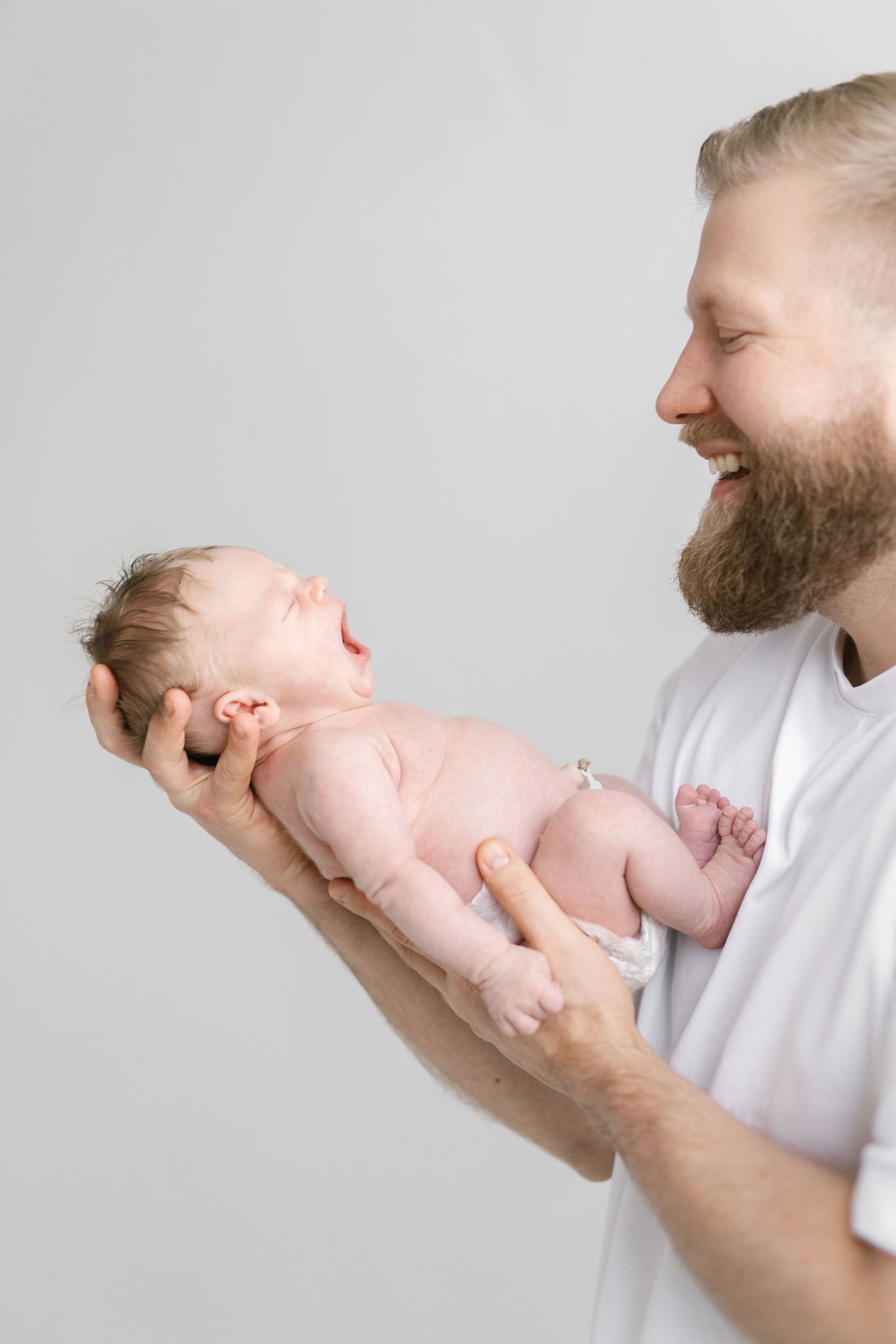 Parent holding and admiring newborn baby against light background.