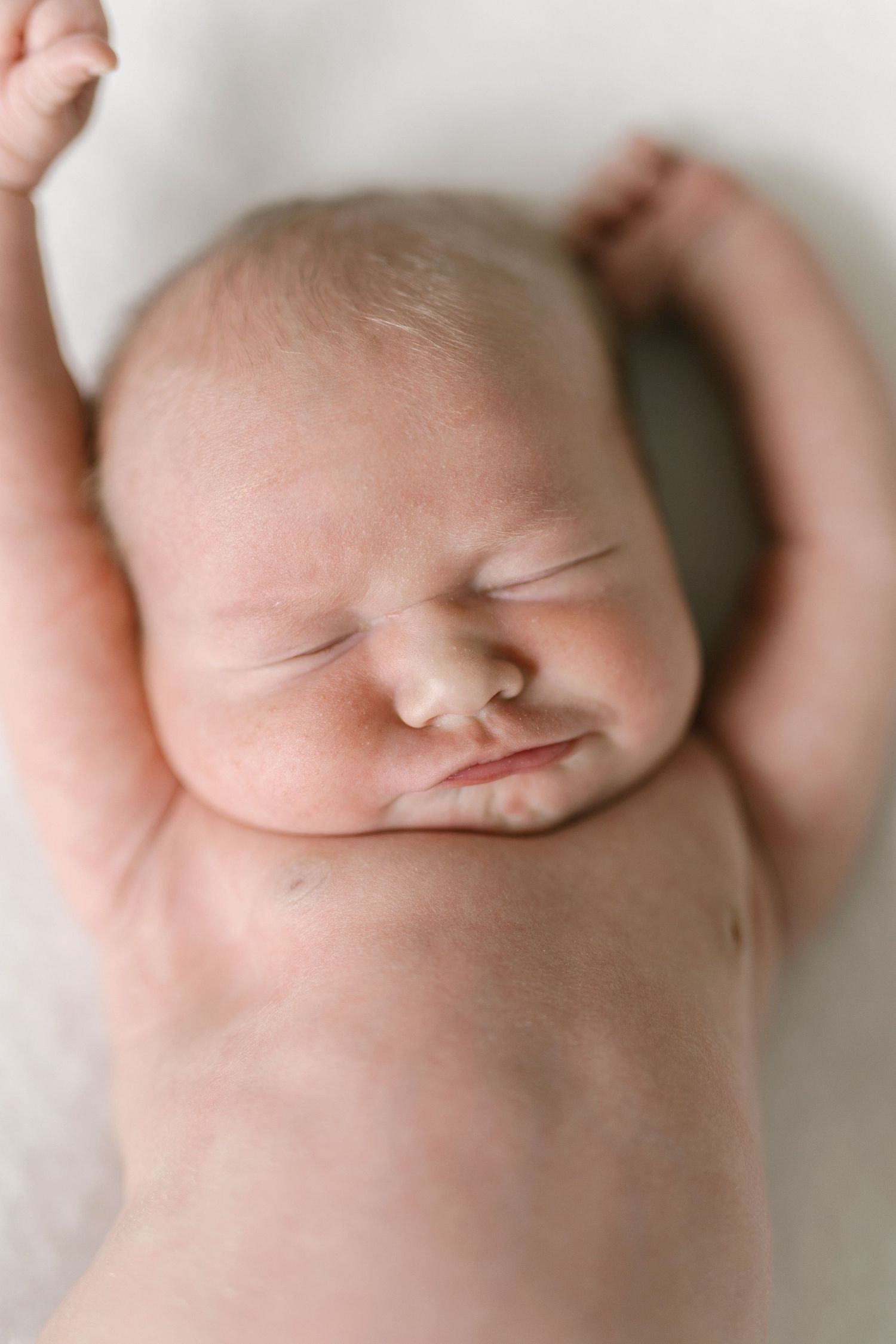 Peaceful sleeping newborn baby lying on white background with arms raised, captured in soft natural light.
