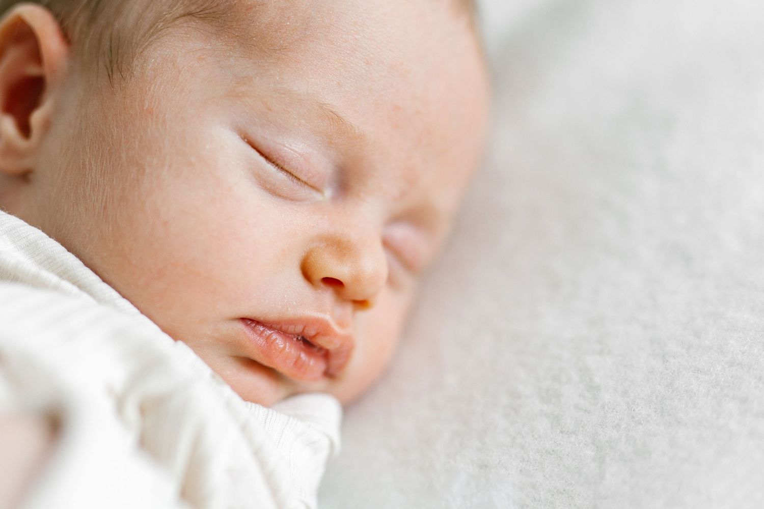 Peaceful newborn baby sleeping on a soft white blanket, with delicate features and gentle skin tones.