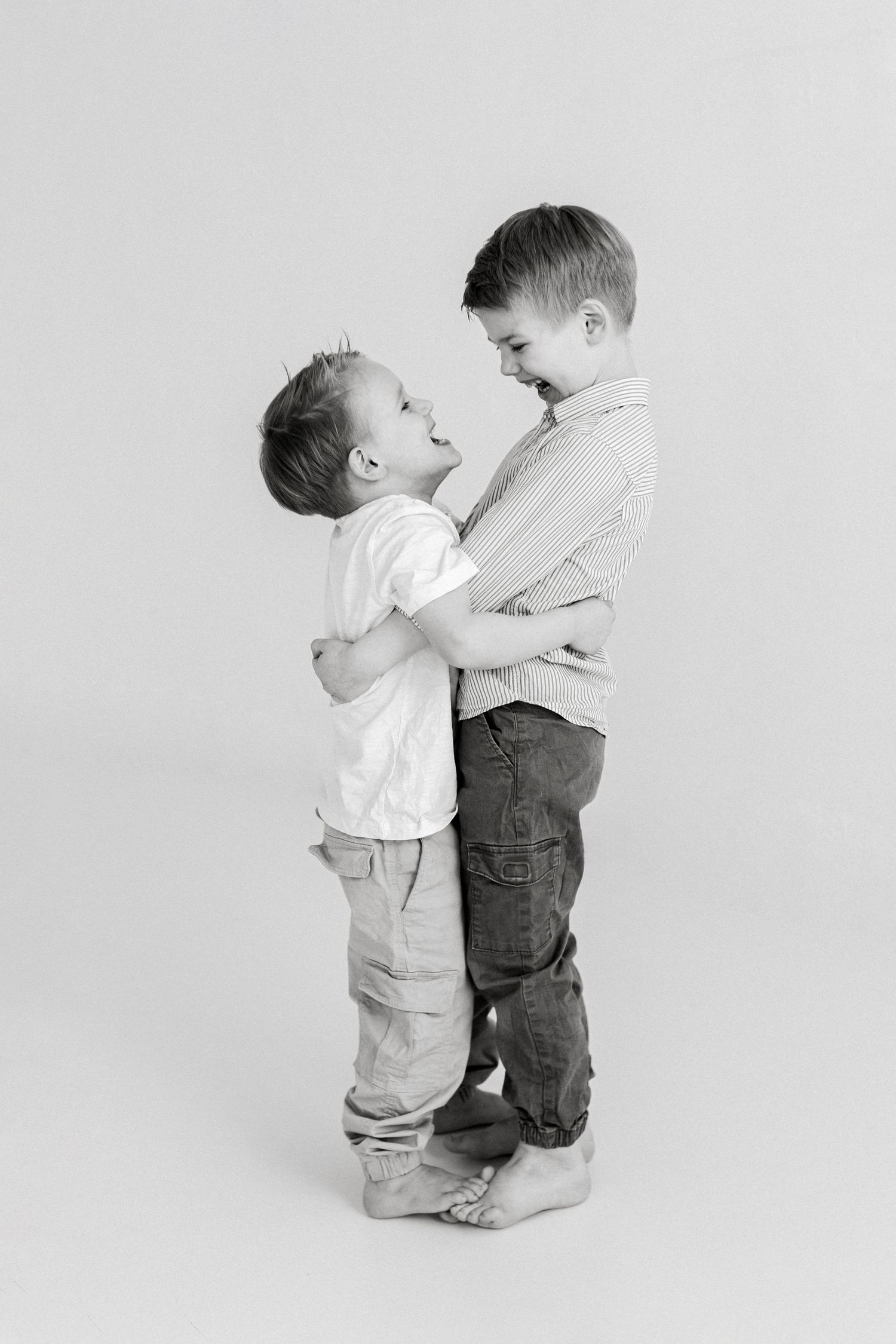 Two young children in casual clothing interact playfully against a white background in a series of black and white photos.